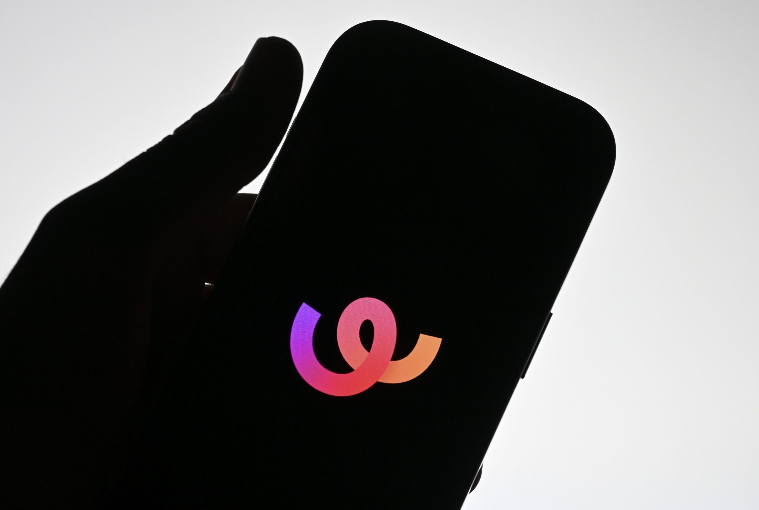 The silhouette of a hand holding a phone that displays the Whee logo. 