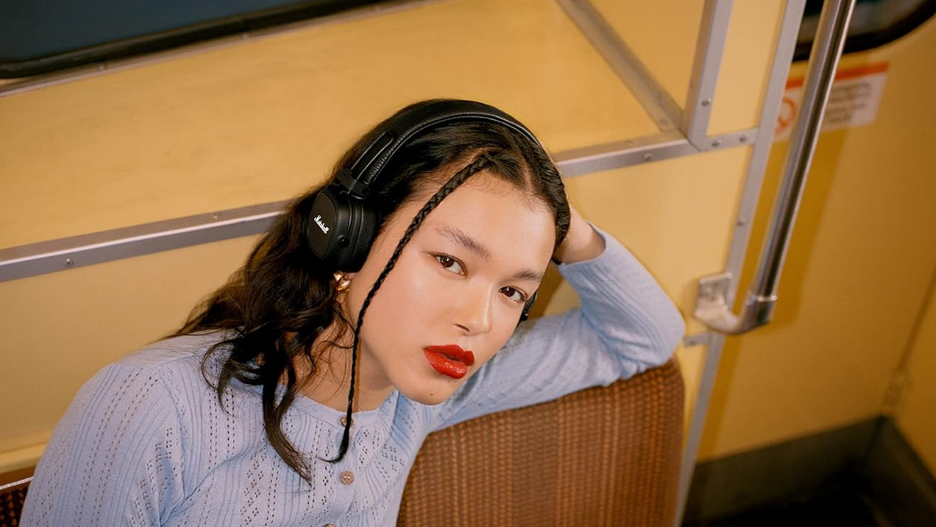 A person sitting on a train wearing Marshall Major IV headphones