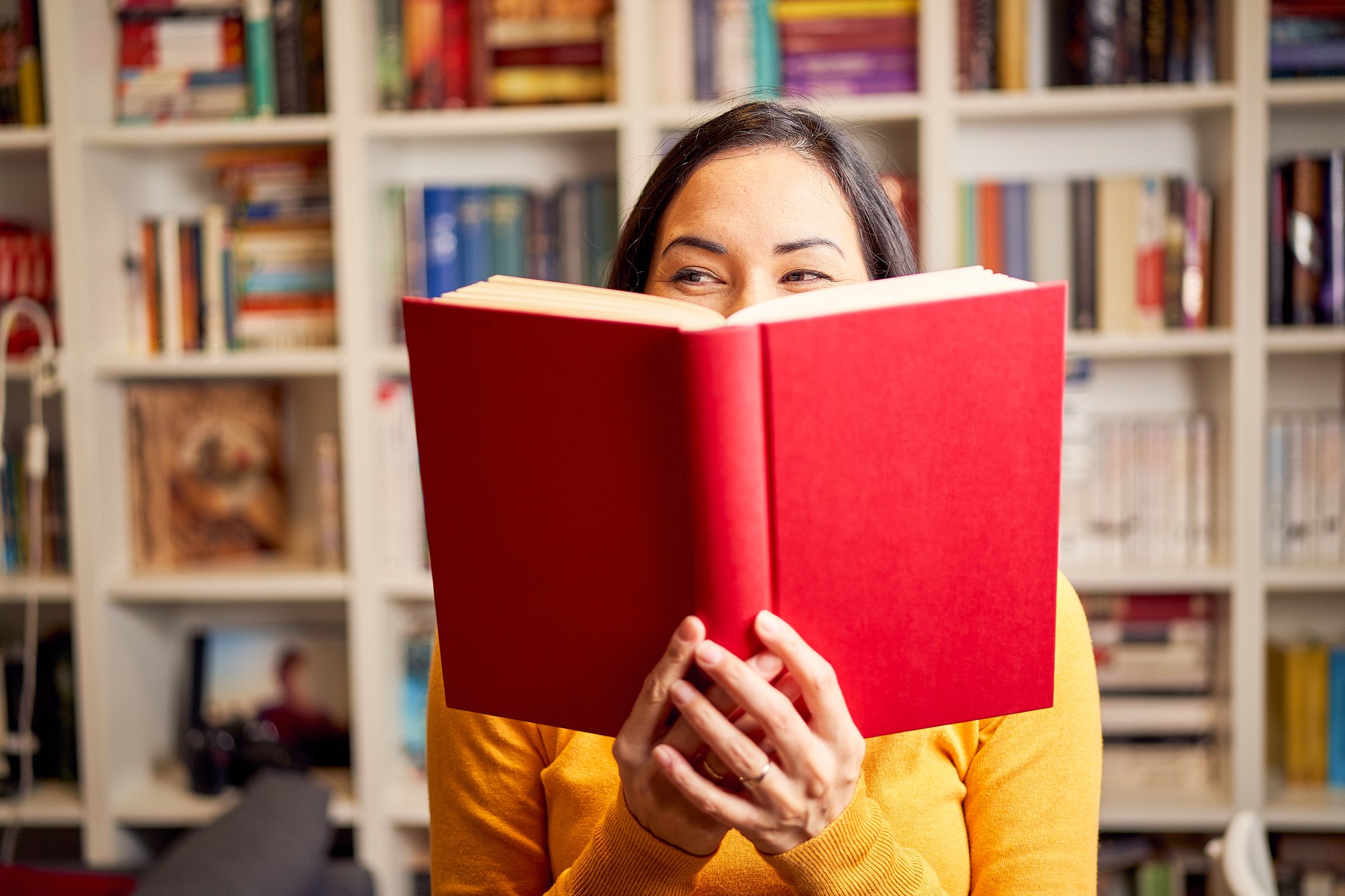 A woman poses with a book in front of a book shelf