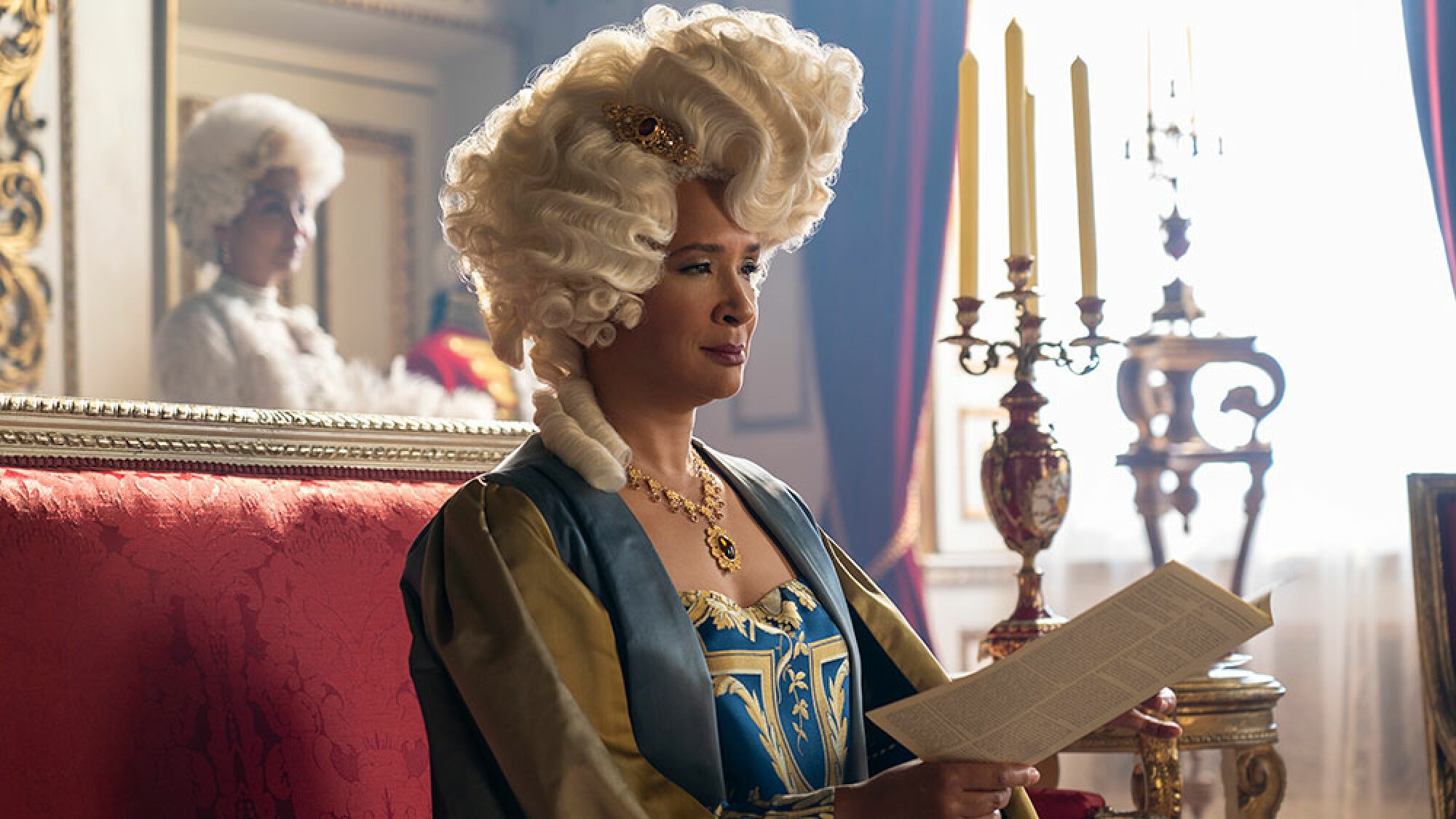 A woman in regal attired reads a pamphlet while sitting down.