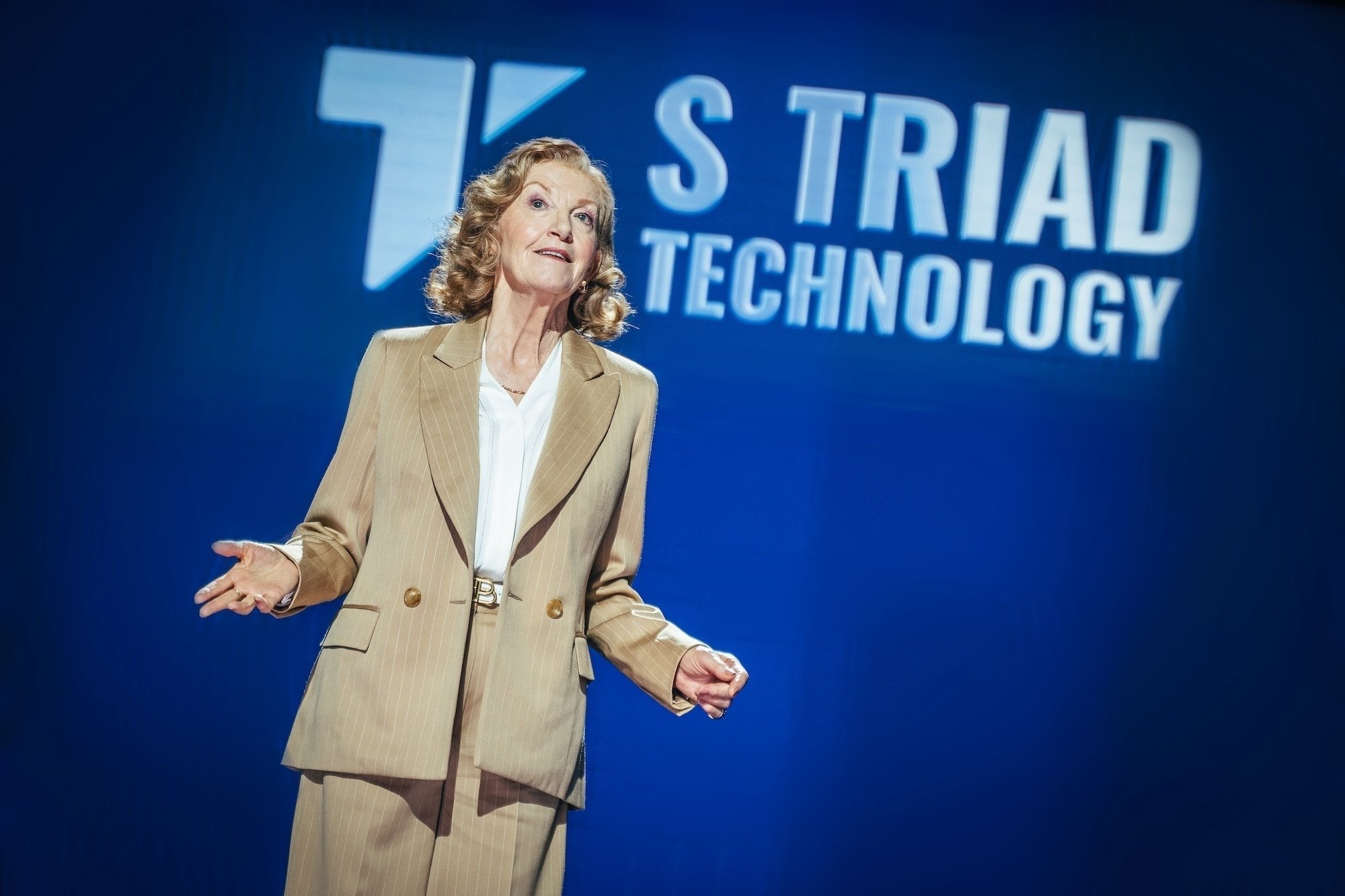 A woman in a business suit standing in front of the "S Triad" corporate logo.