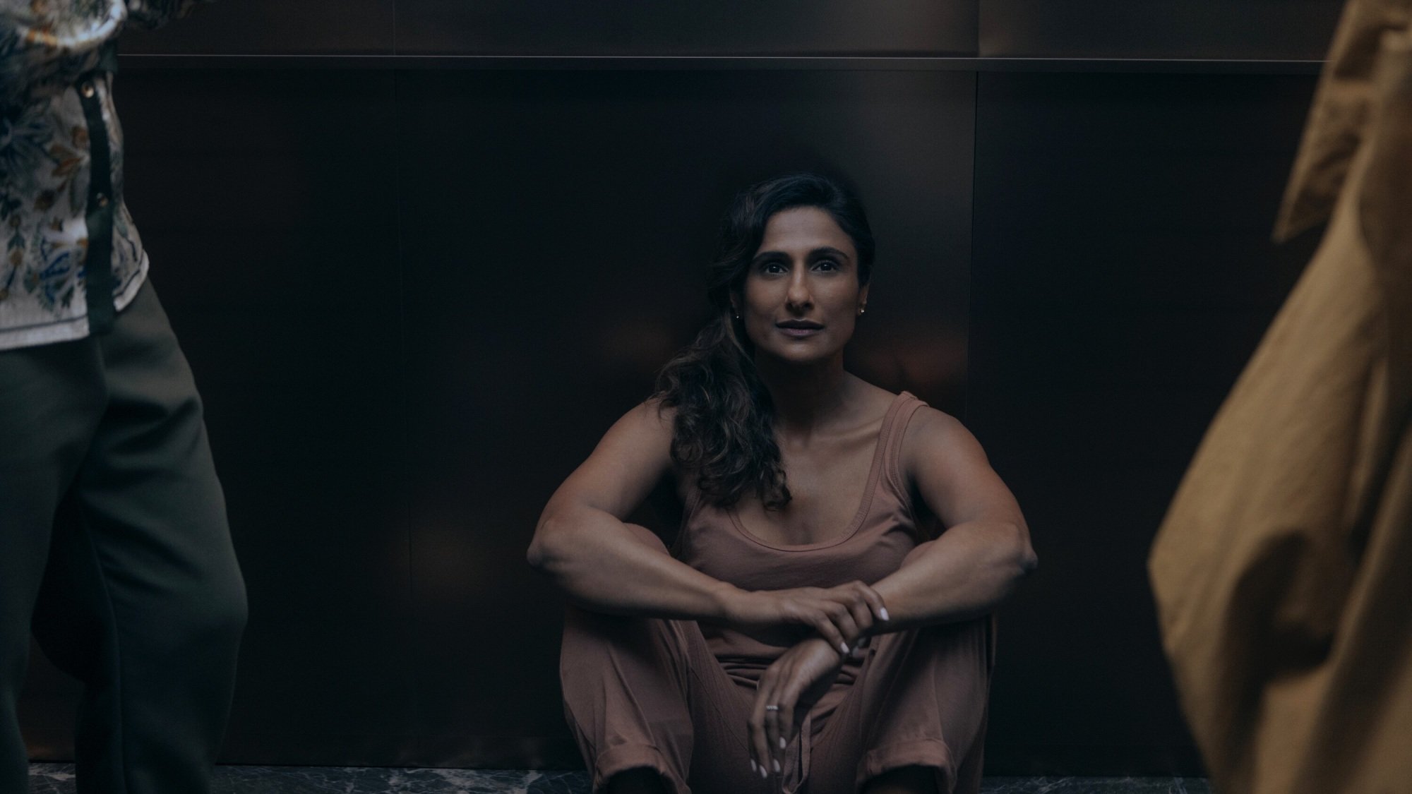 A woman sits on the floor of an elevator between two other women, who are standing.