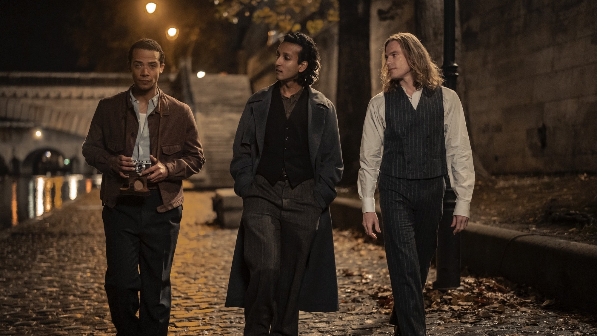 Three men walk along the banks of the Seine at night.