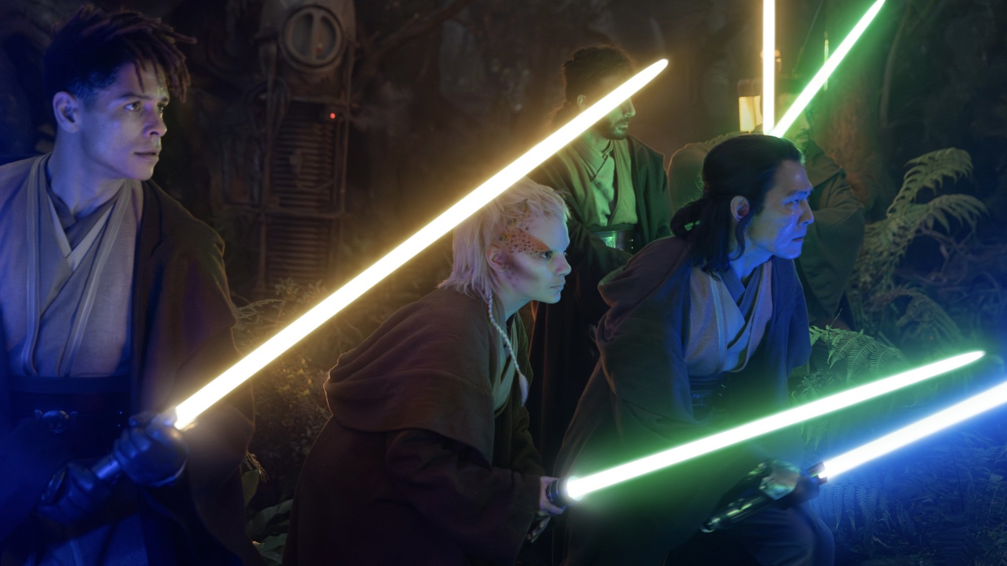 Yord, Jecki, and Sol from "The Acolyte" rush into battle in a dark forest, their lightsabers aglow.