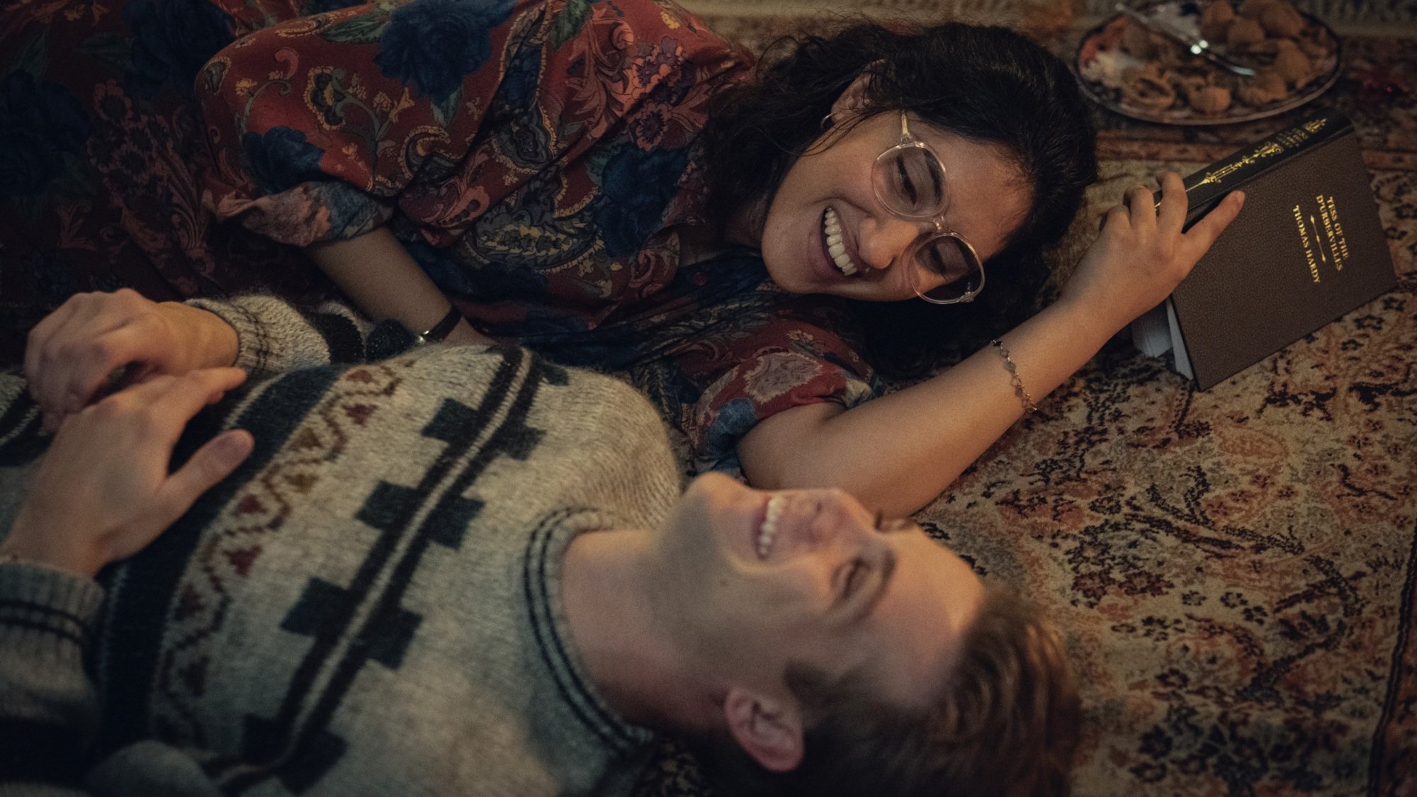 A man and woman lie on a carpet, laughing.