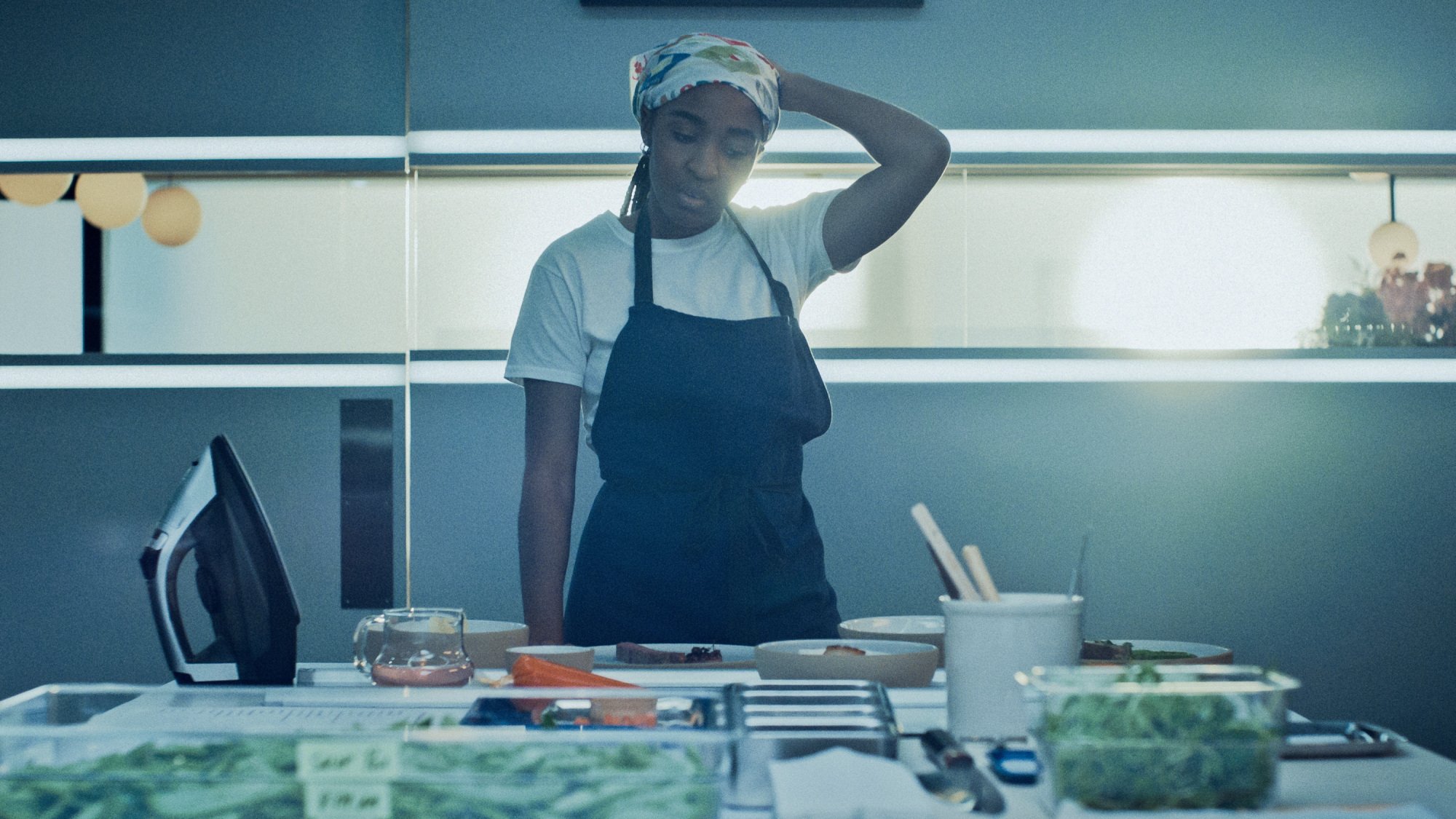 Sydney from "The Bear" stands in a restaurant kitchen overseeing the preparation of food.