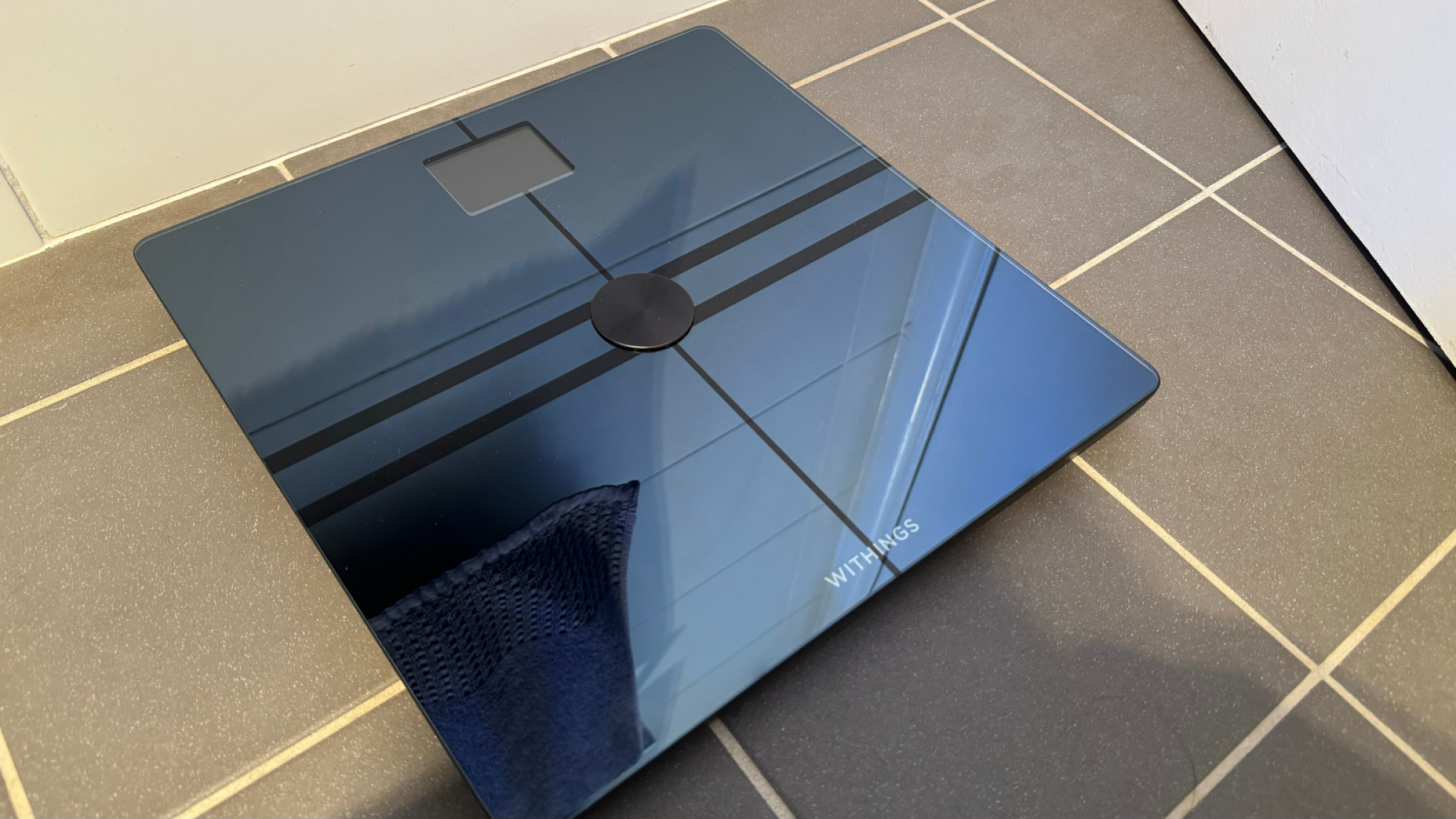 The Withings Body Comp smart scale on a tiled floor.