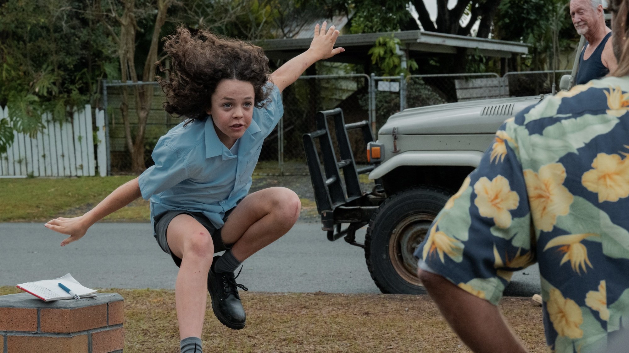 A young boy jumps in the air in a driveway.