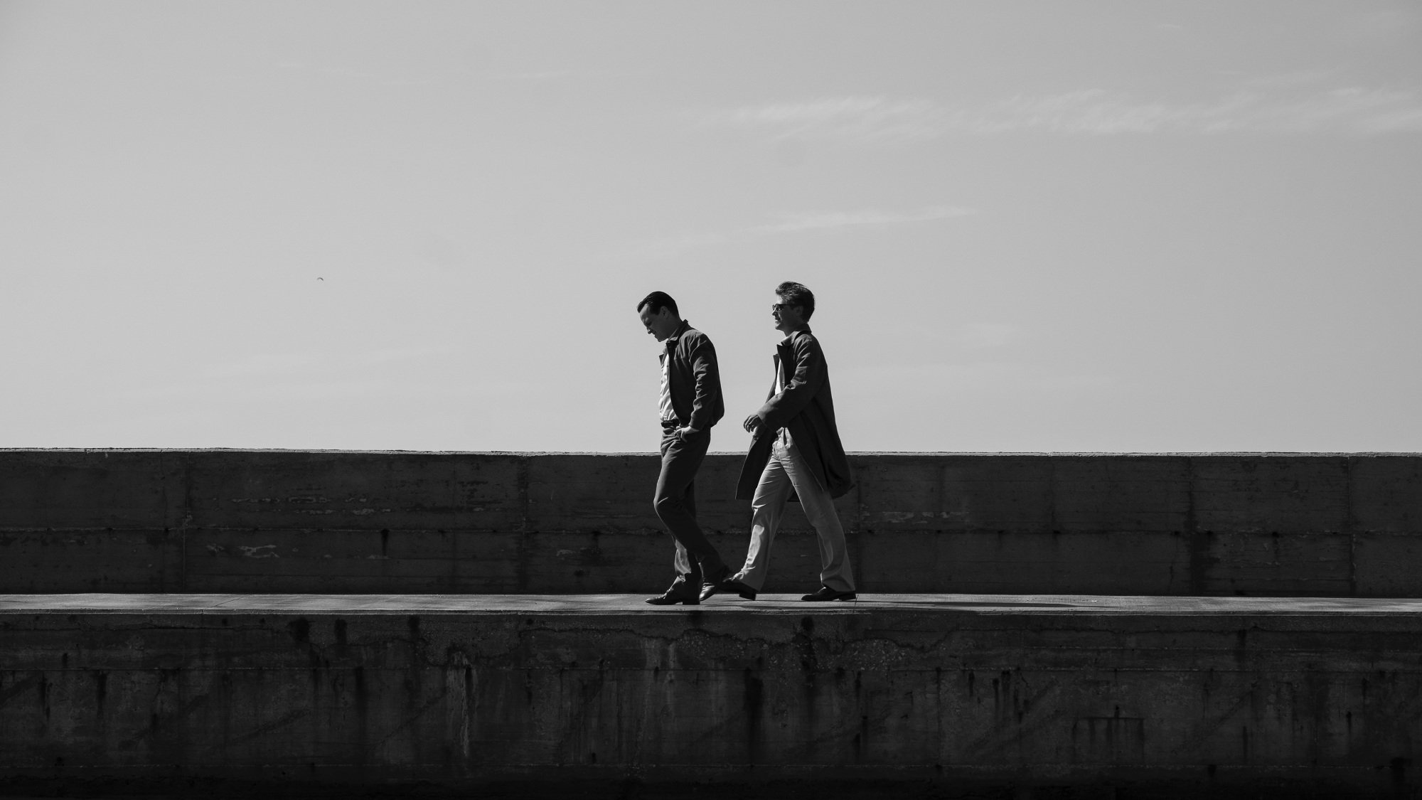 Two men walking along a wall.