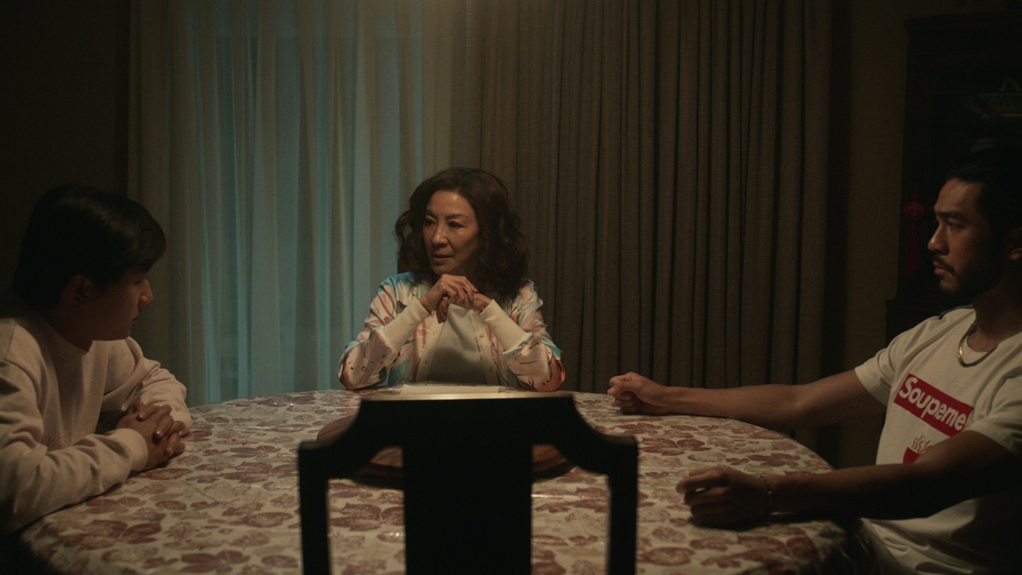 Two brothers sit at opposite sides of a circular table, with their mother between them.