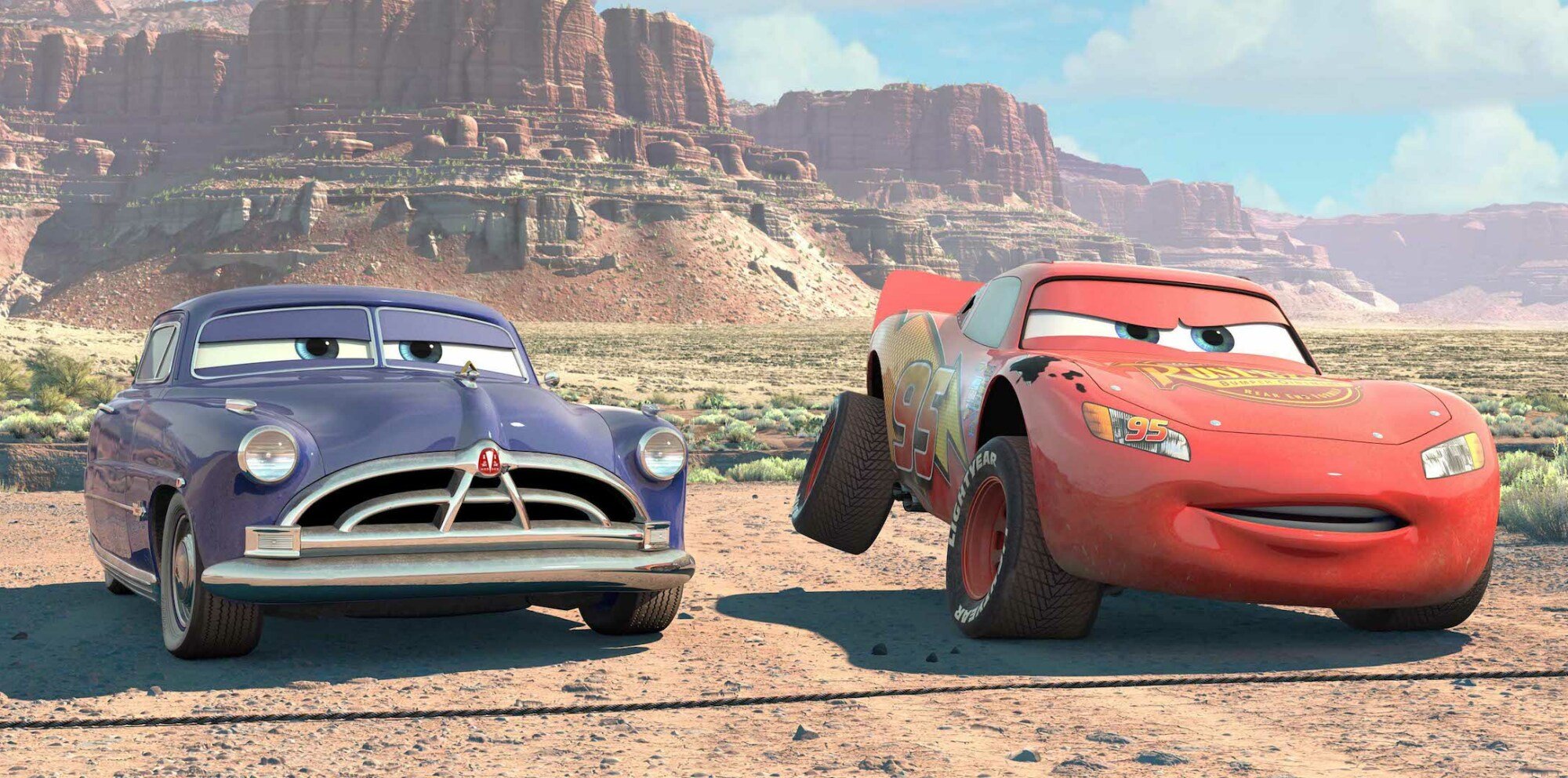 Animated still of two anthropomorphized cars (windshields as eyes) in the desert; one blue, one red.