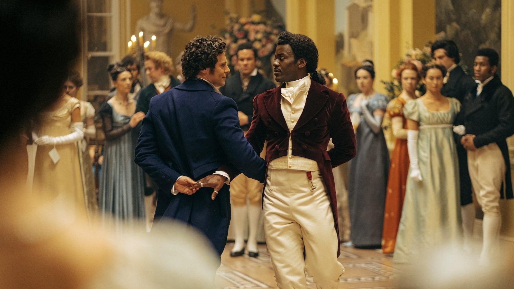 Two men in Regency-era attire dance at a large ball.