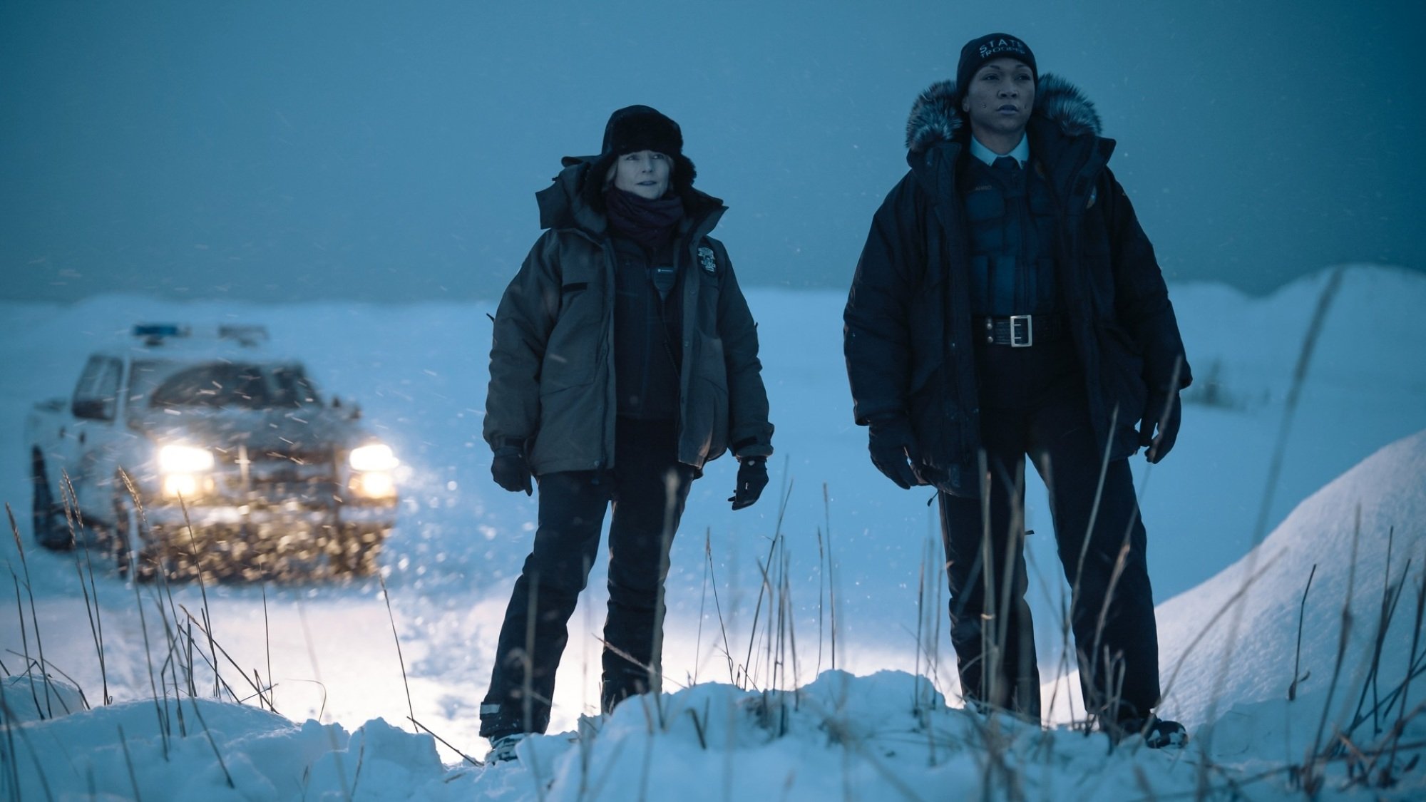 Two women in police uniforms and heavy coats stand in a snowy landscape.