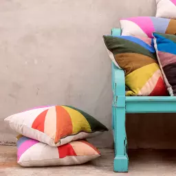 A stack of rainbow pillows next to a teal bench