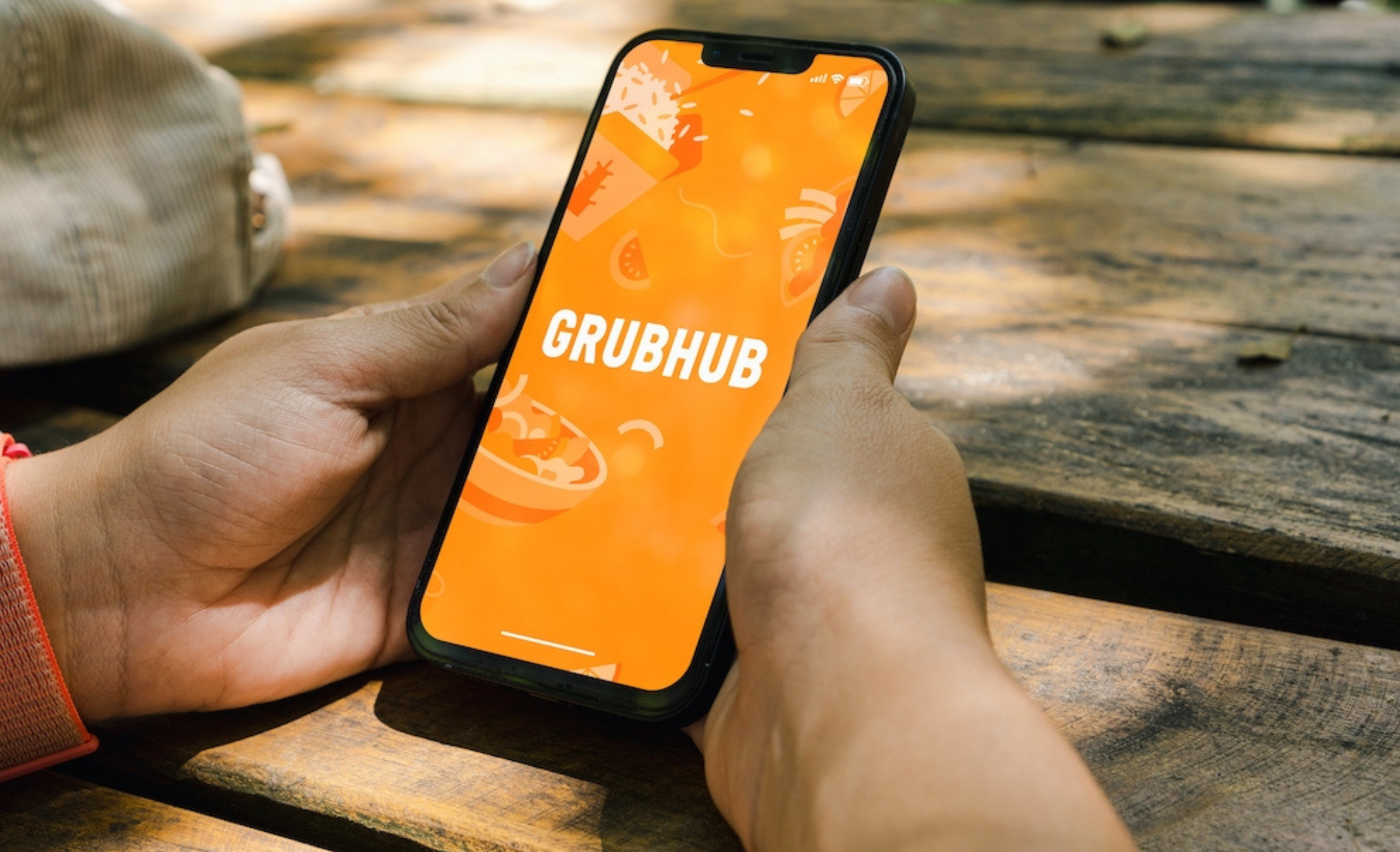 Girl in the park holding a smartphone with GrubHub food ordering and deliveryapp on the screen. Rustic wooden table. Rio de Janeiro, RJ, Brazil. July 2022.