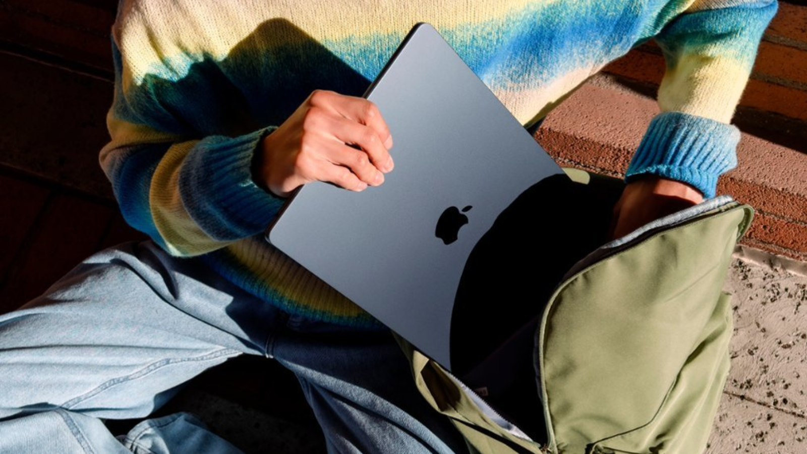 a close-up of a person putting an m3 apple macbook air into a backpack