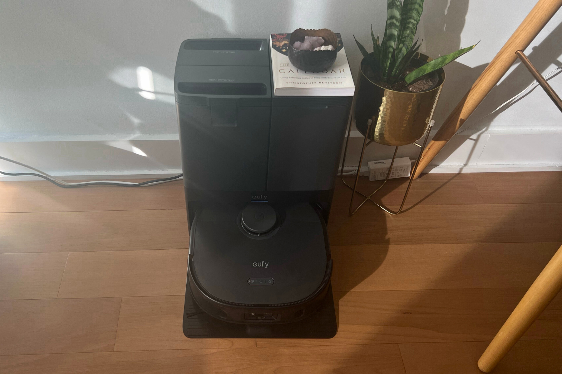 Eufy X10 Pro Omni robot vacuum and dock sitting on hardwood floor against will with potted plant and desk in peripherals