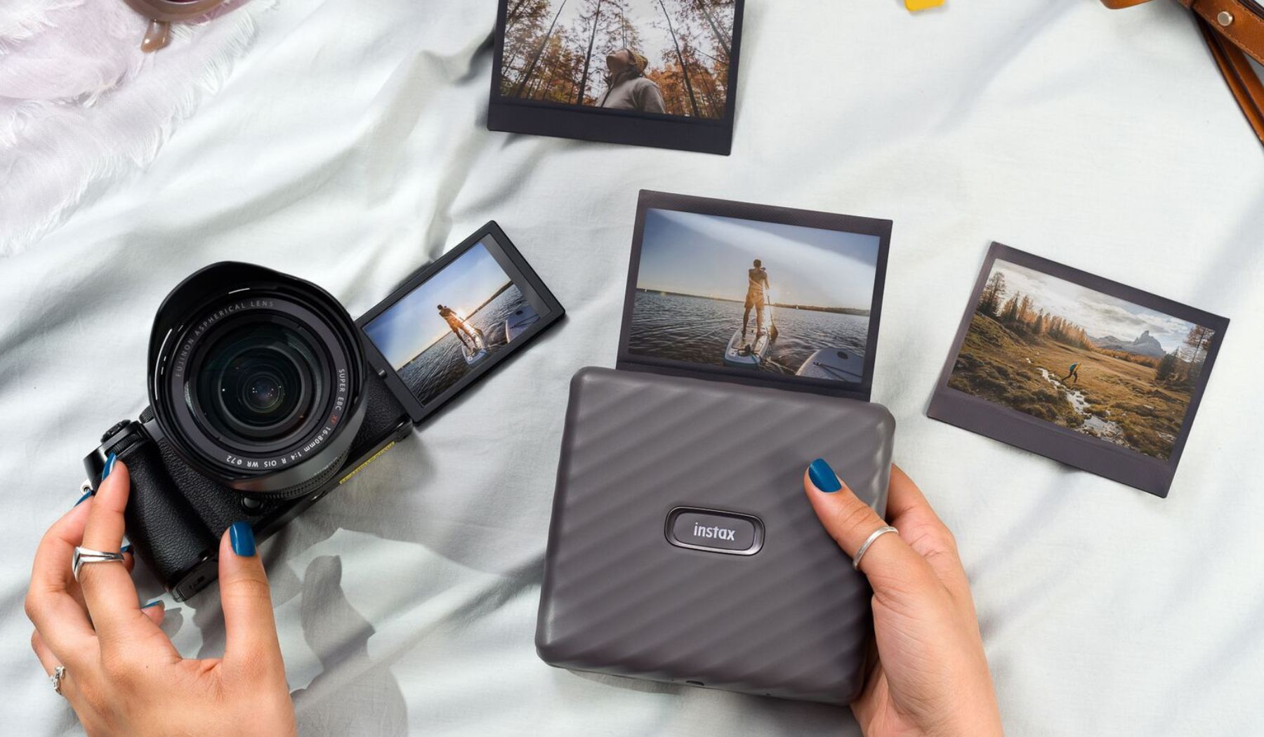 Person's hands using mirrorless camera and portable photo printer with scattered printed photos and fabric in peripherals