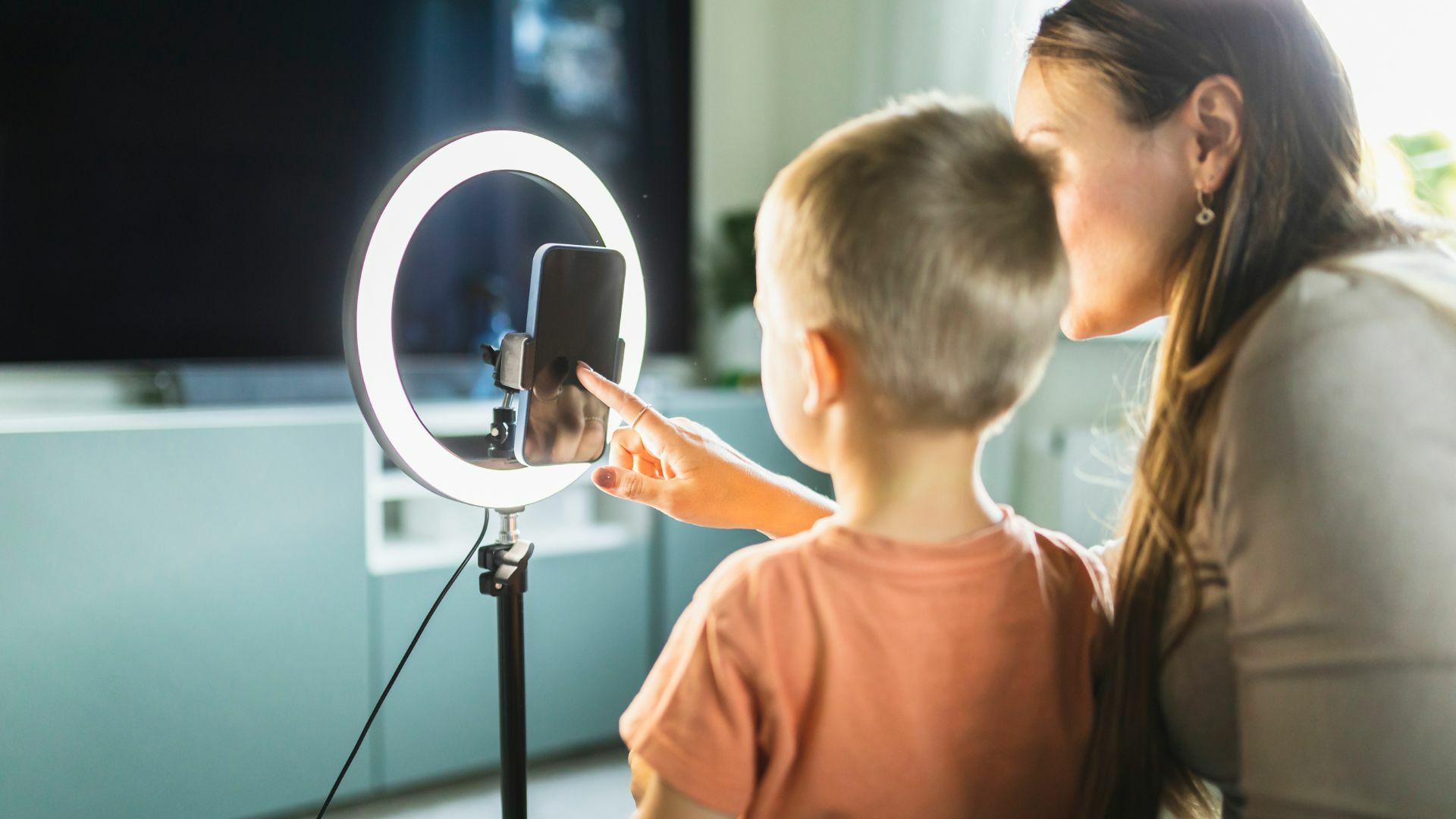 Mother live streaming with son on smart phone with ring light at home.