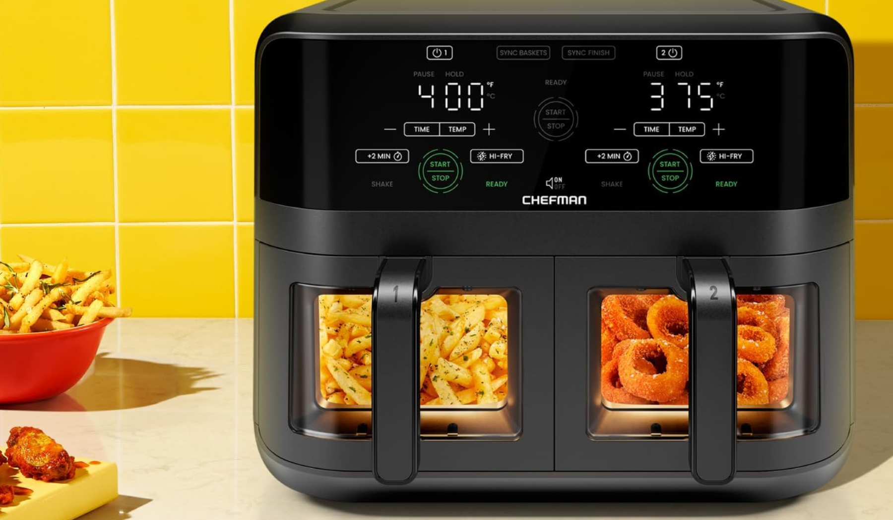 Chefman air fryer with fries and onion rings in baskets and other fried appetizers on counter beside it