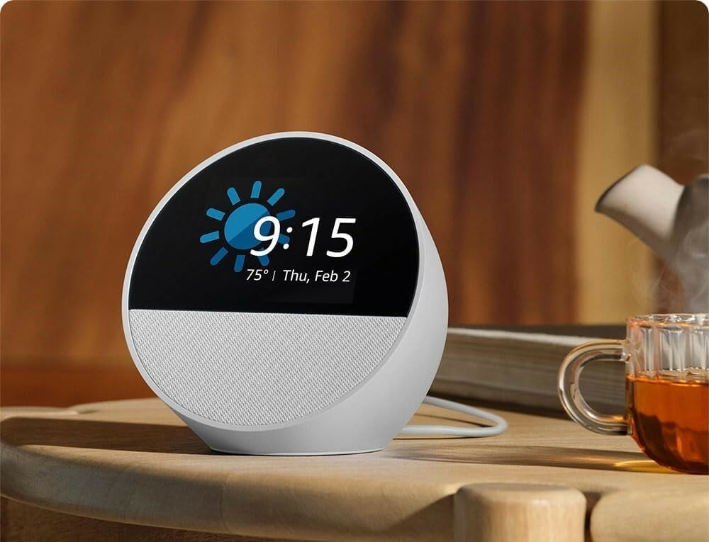 the amazon echo spot shows the time while sitting on a table with a cup of tea beside it