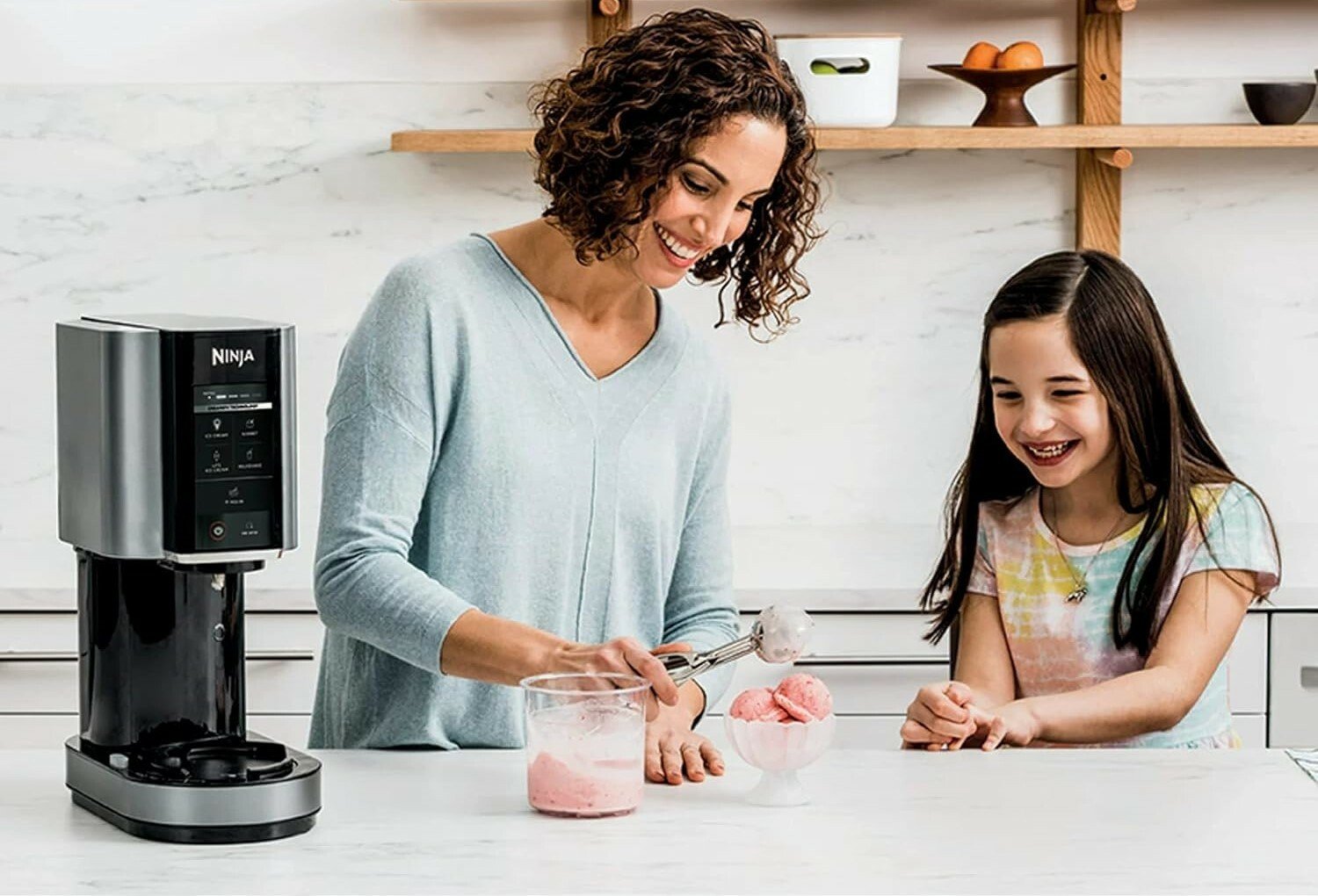 a mom makes ice cream with the ninja creami machine while daughter looks on smiling