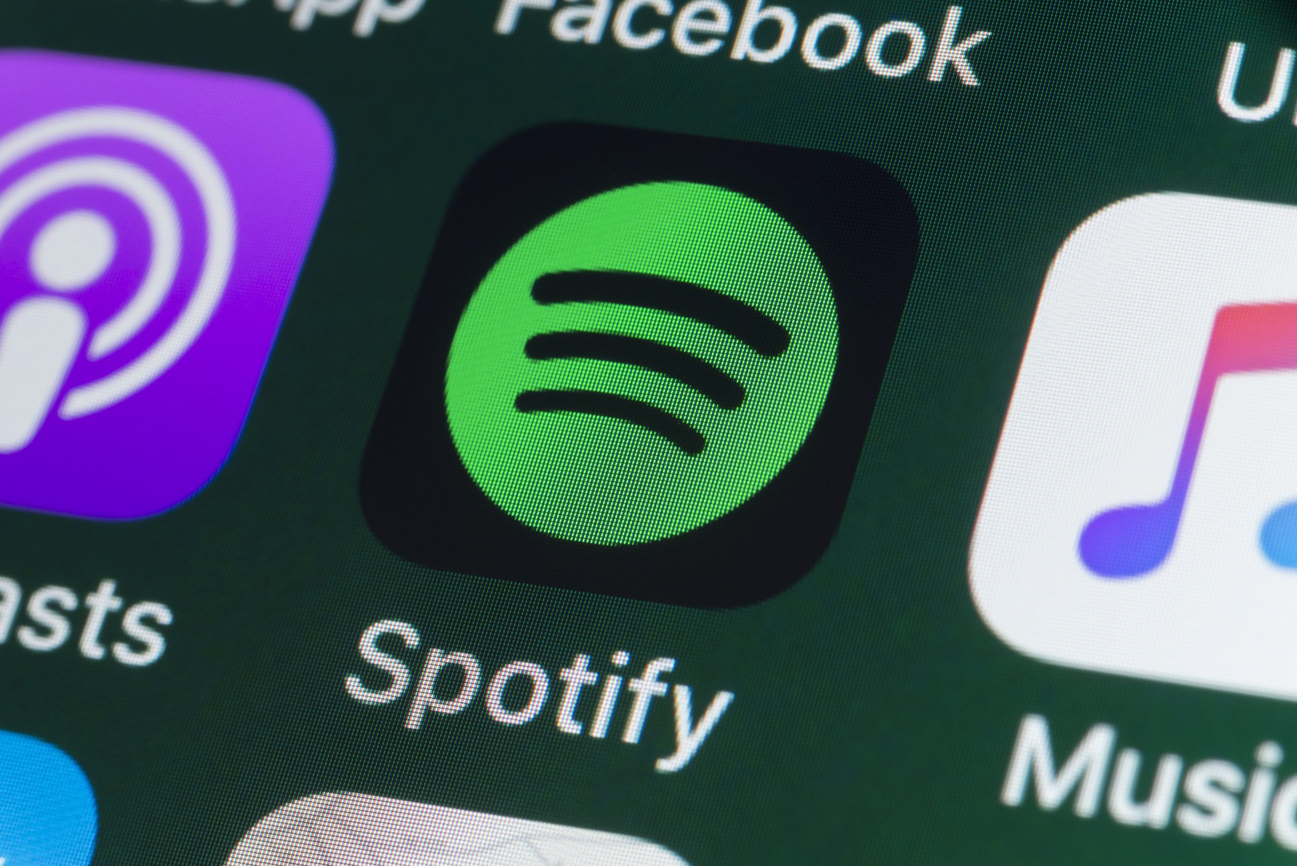 he buttons of the music streaming app Spotify, surrounded by Podcasts, Apple Music, Facebook and other apps on the screen of an iPhone.