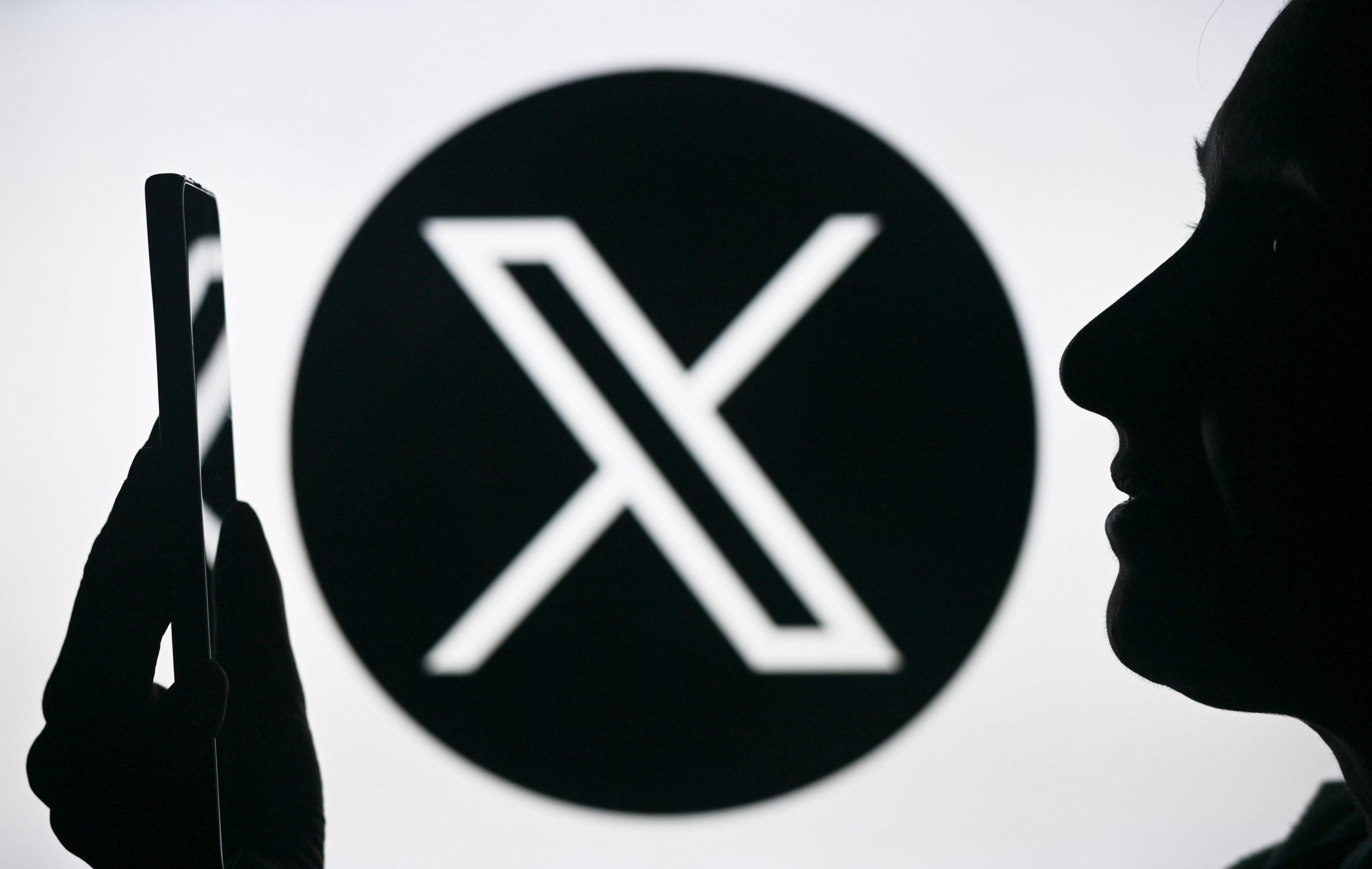 X logo behind user on smartphone