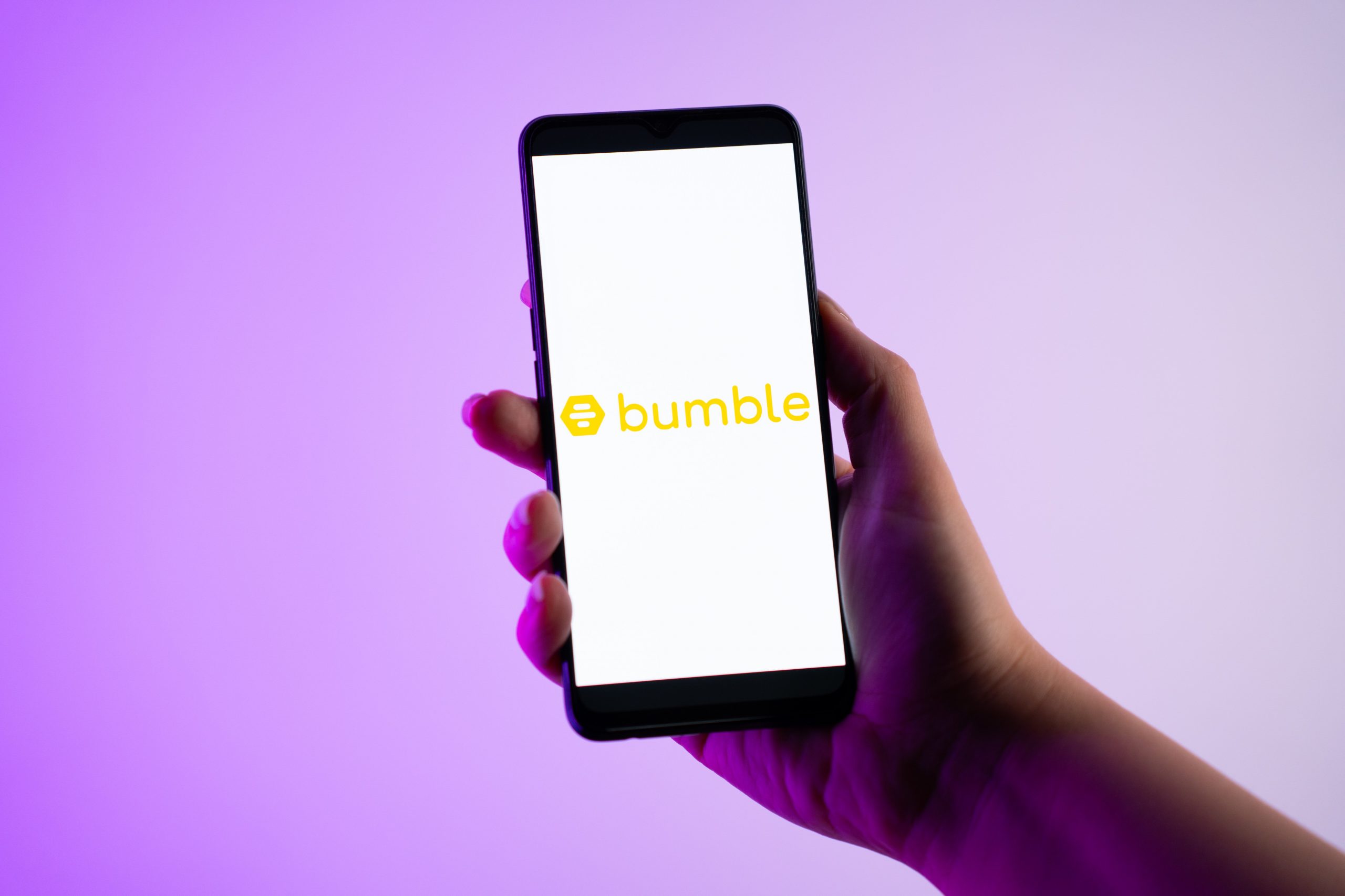 A person is holding a mobile phone with the Bumble dating app logo on its screen