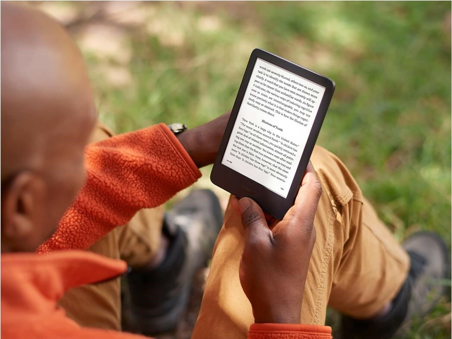 a person reads on a kindle e-reader while sitting on the ground outside