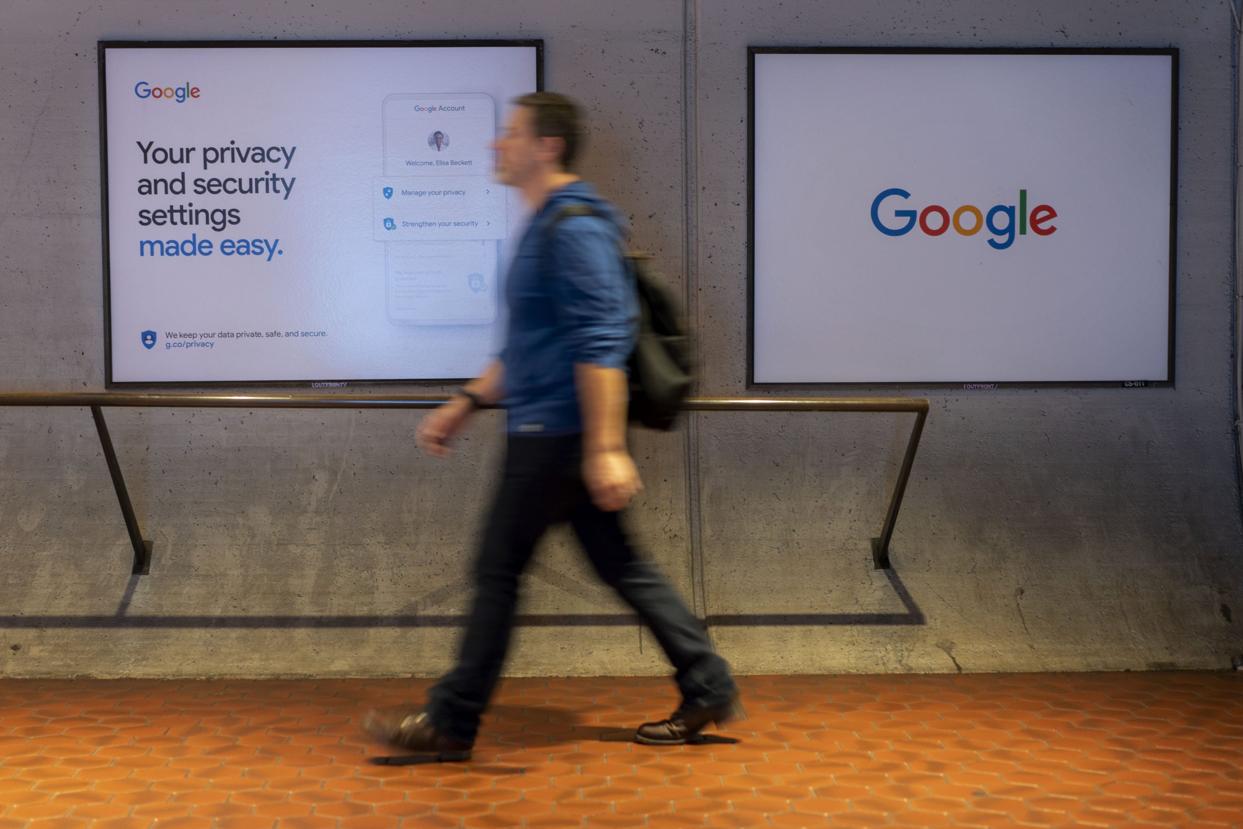 A person walks in front of a screen with the Google logo, and another with a Google privacy slogan