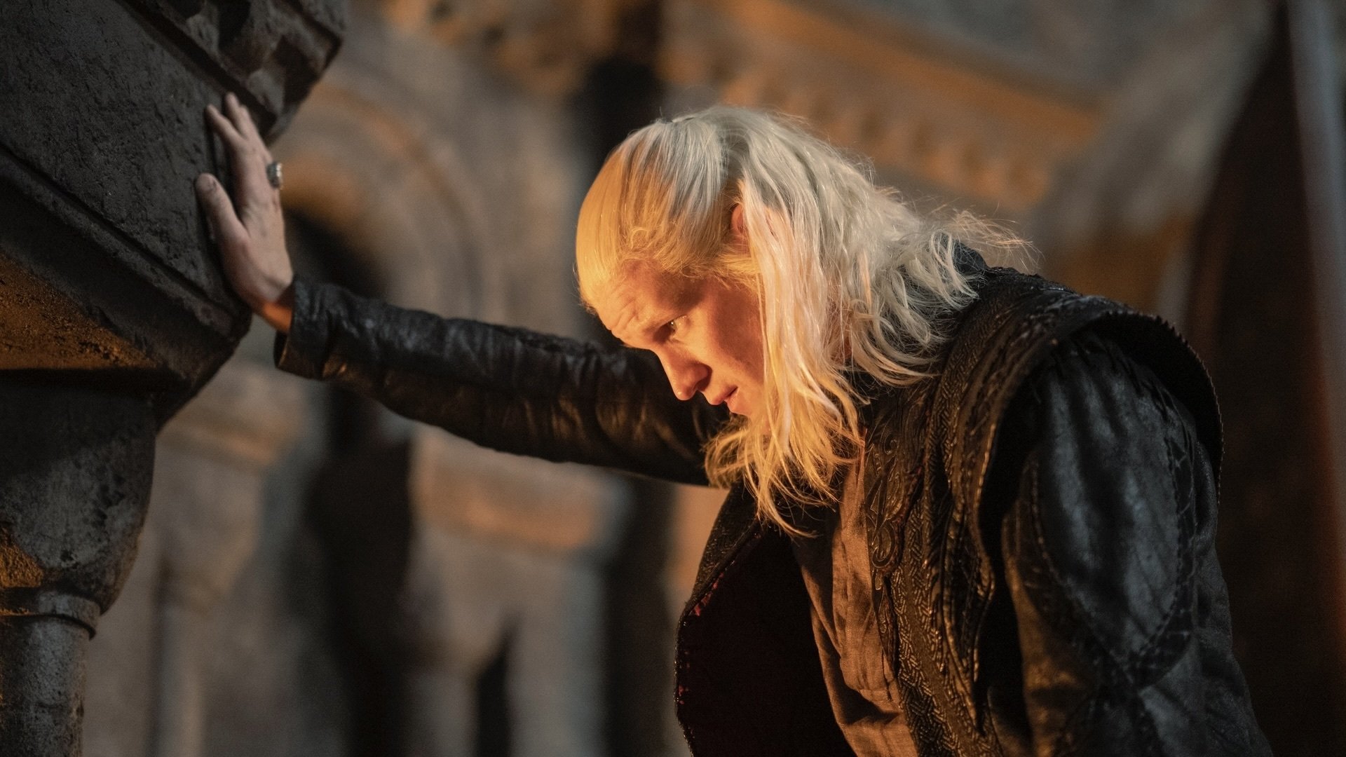 Daemon Targaryen braces himself against a wall with one hand, staring deep into a fireplace.