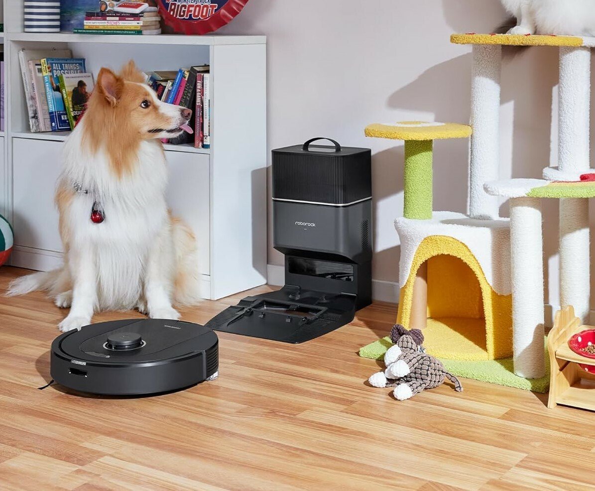 A Roborock robot vacuum cleans up pet hair in a playroom next to a dog