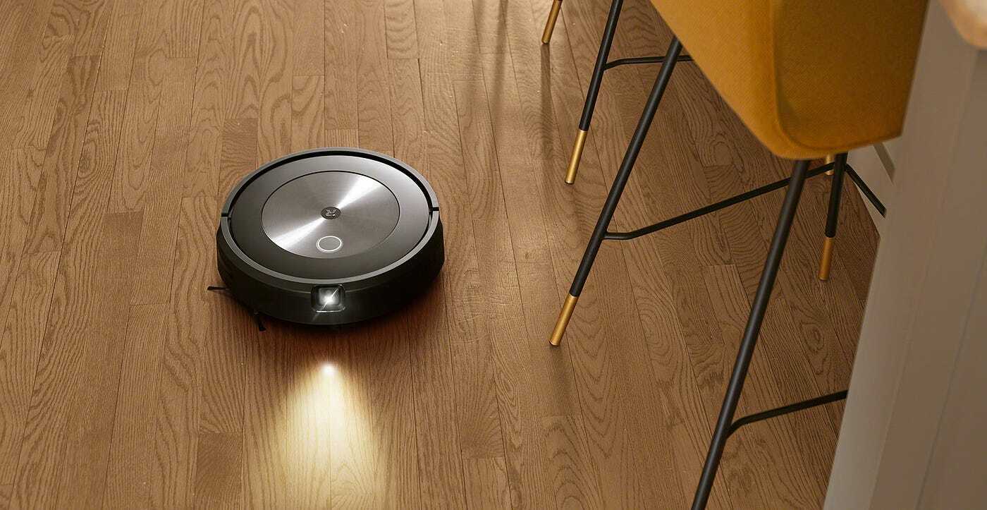 Roomba j7 robot vacuum cleaning hardwood floor with kitchen chair legs in peripherals