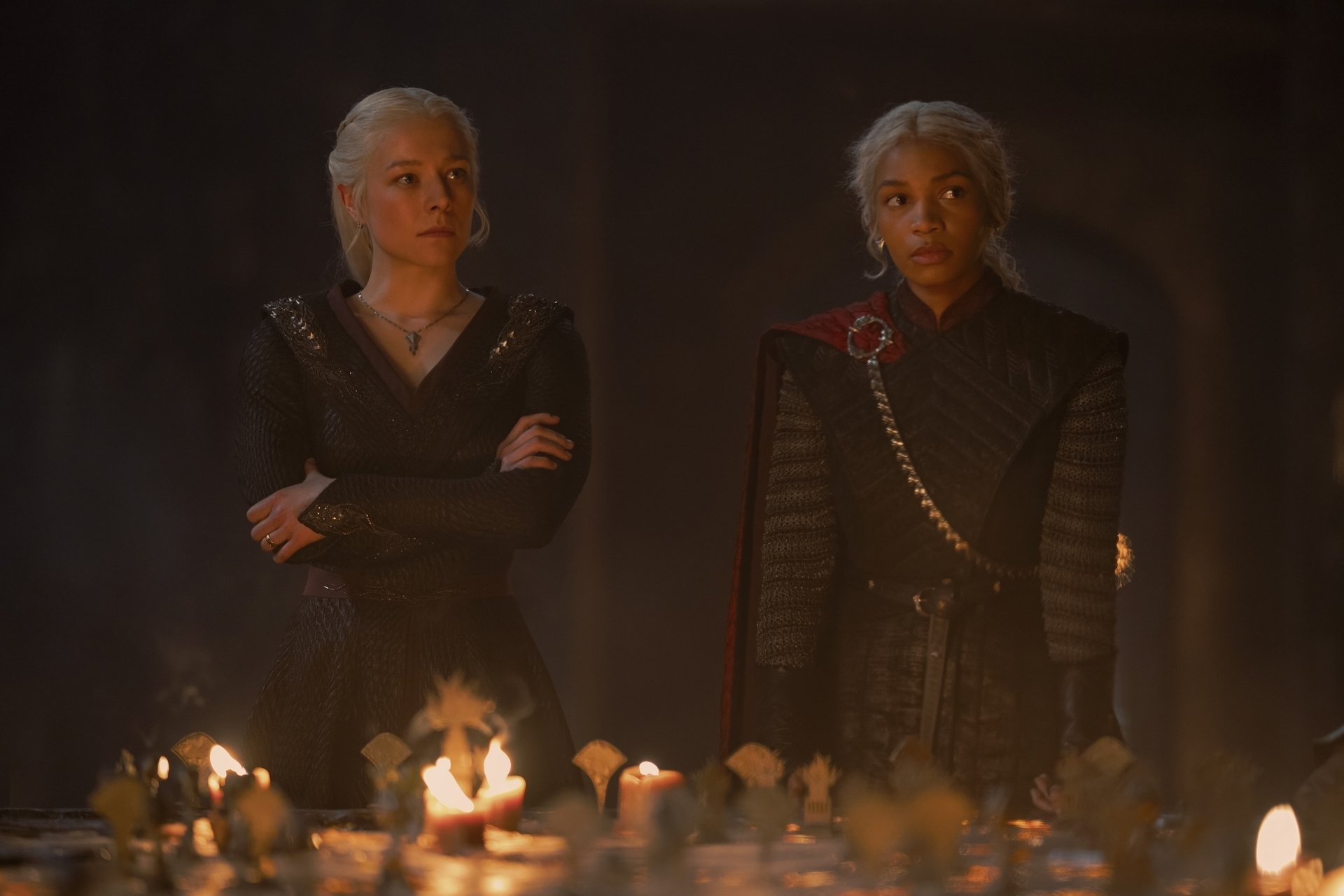 Rhaenyra and Baela Targaryen stand at the head of a war table covered in candles.