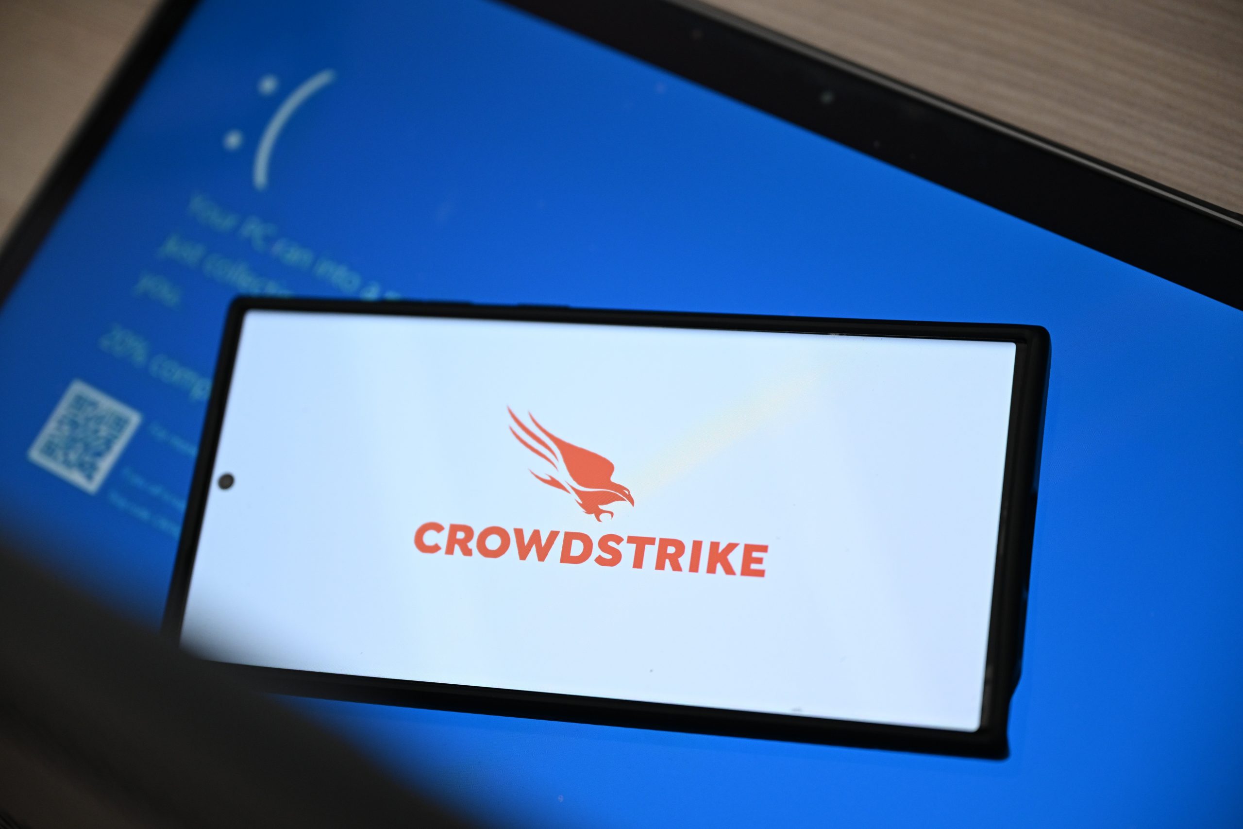 CrowdStrike logo on smartphone on top of Windows blue screen of death