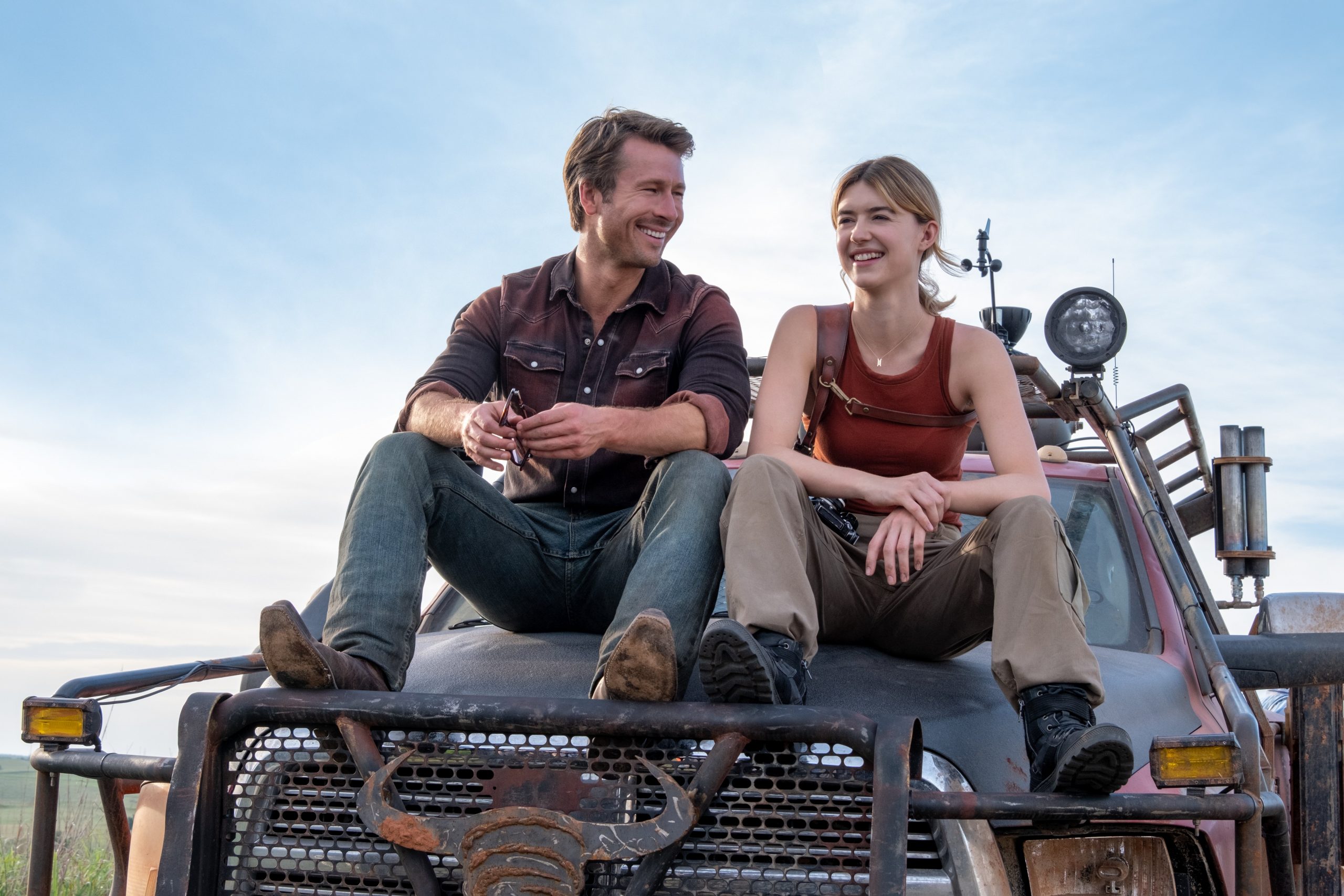 Tyler (Glen Powell) and Kate (Daisy Edgar-Jones) in a still from Twisters. They are sitting on the hood of a truck.