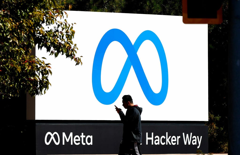 A pedestrian walks in front of a new logo and the name 'Meta' on the sign in front of Facebook headquarters.