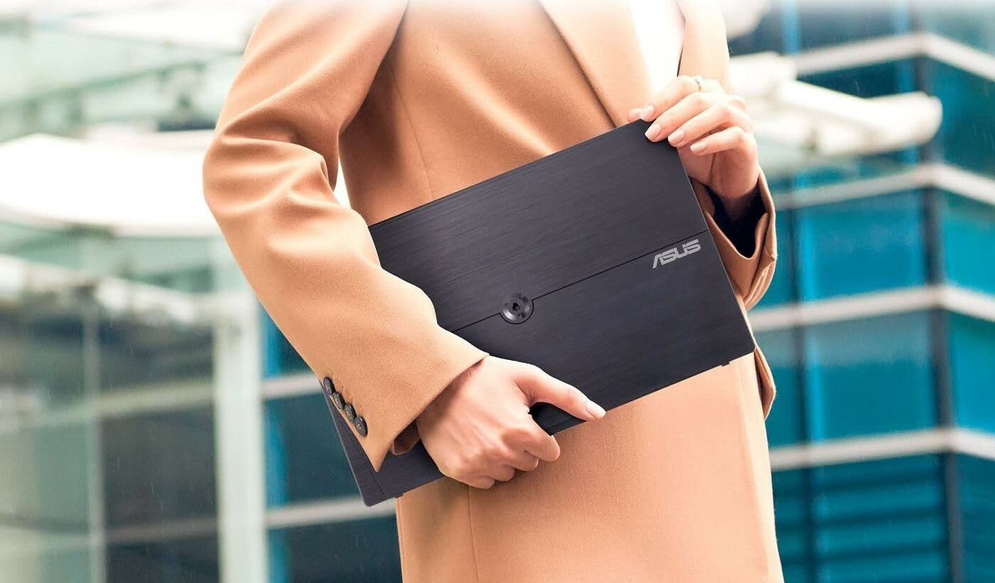 a person wearing a tan colored suit holds the asus zenscreen portable monitor while standing outside of a building