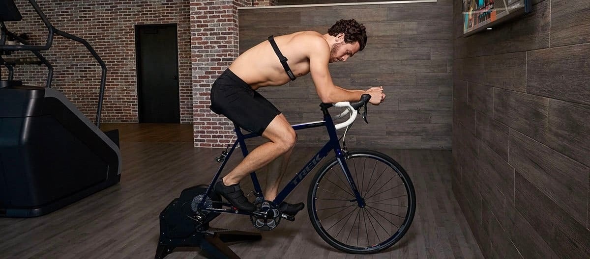 shirtless man wearing chest heart rate monitor on exercise bike