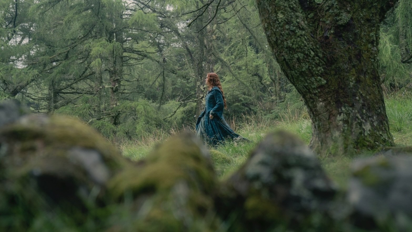 Alicent Hightower walks through the Kingswood in a green dress and cloak.