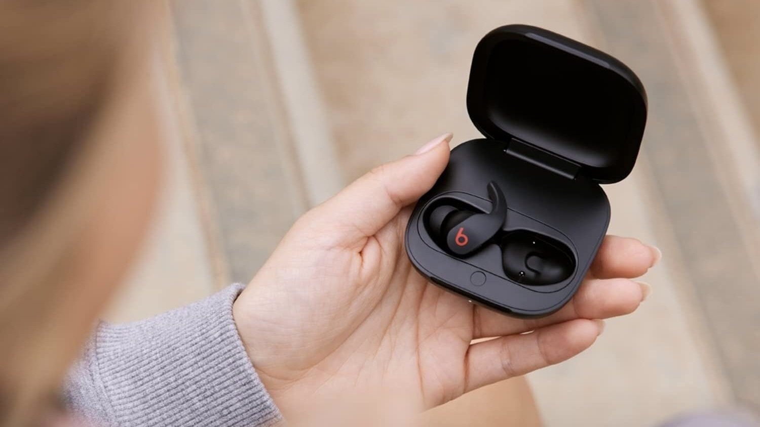 person sitting down outside holding open black beats fit pro case with earbuds inside