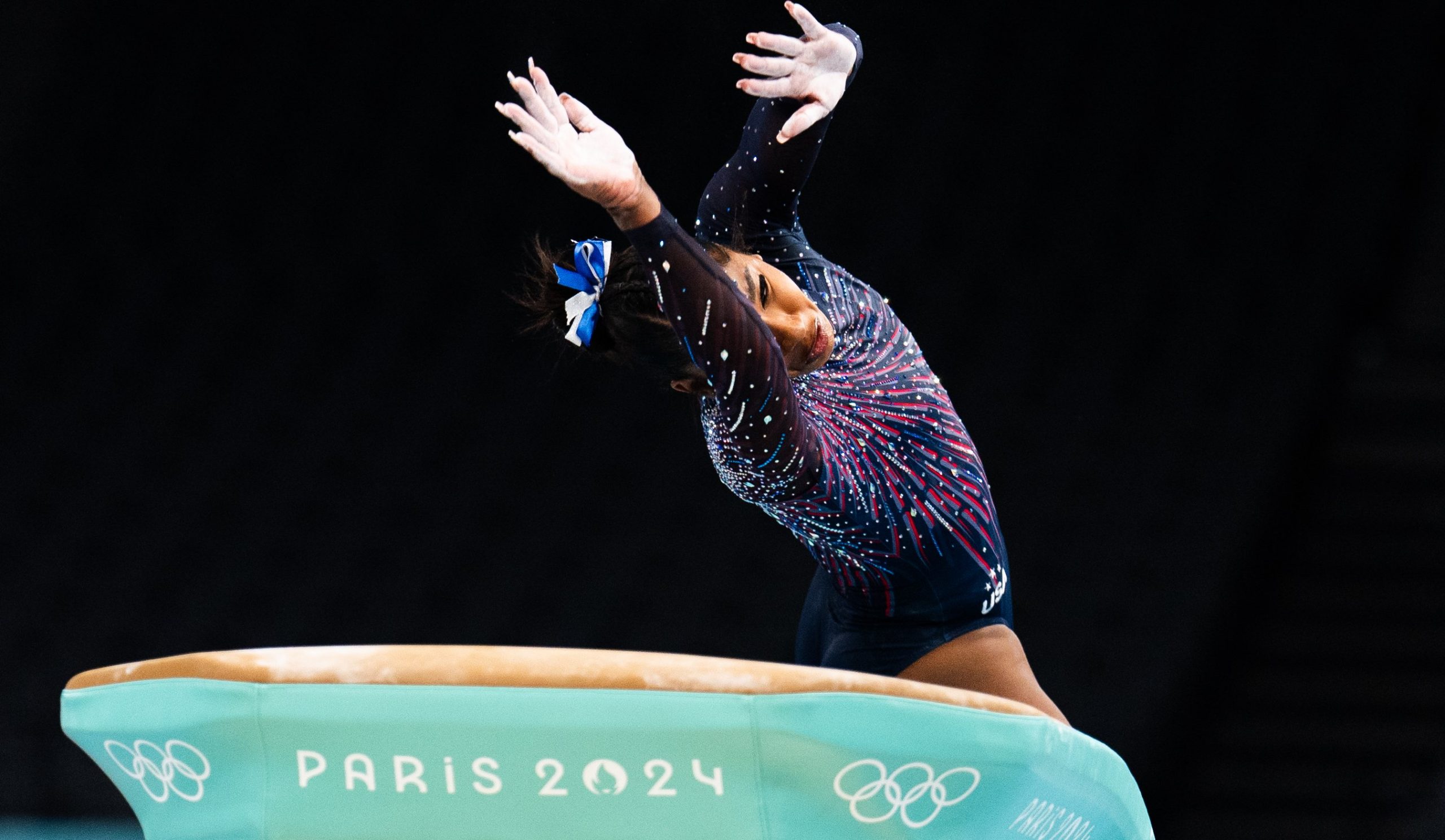 A gymnast twists their body in the air as the float over a green vault apparatus. 