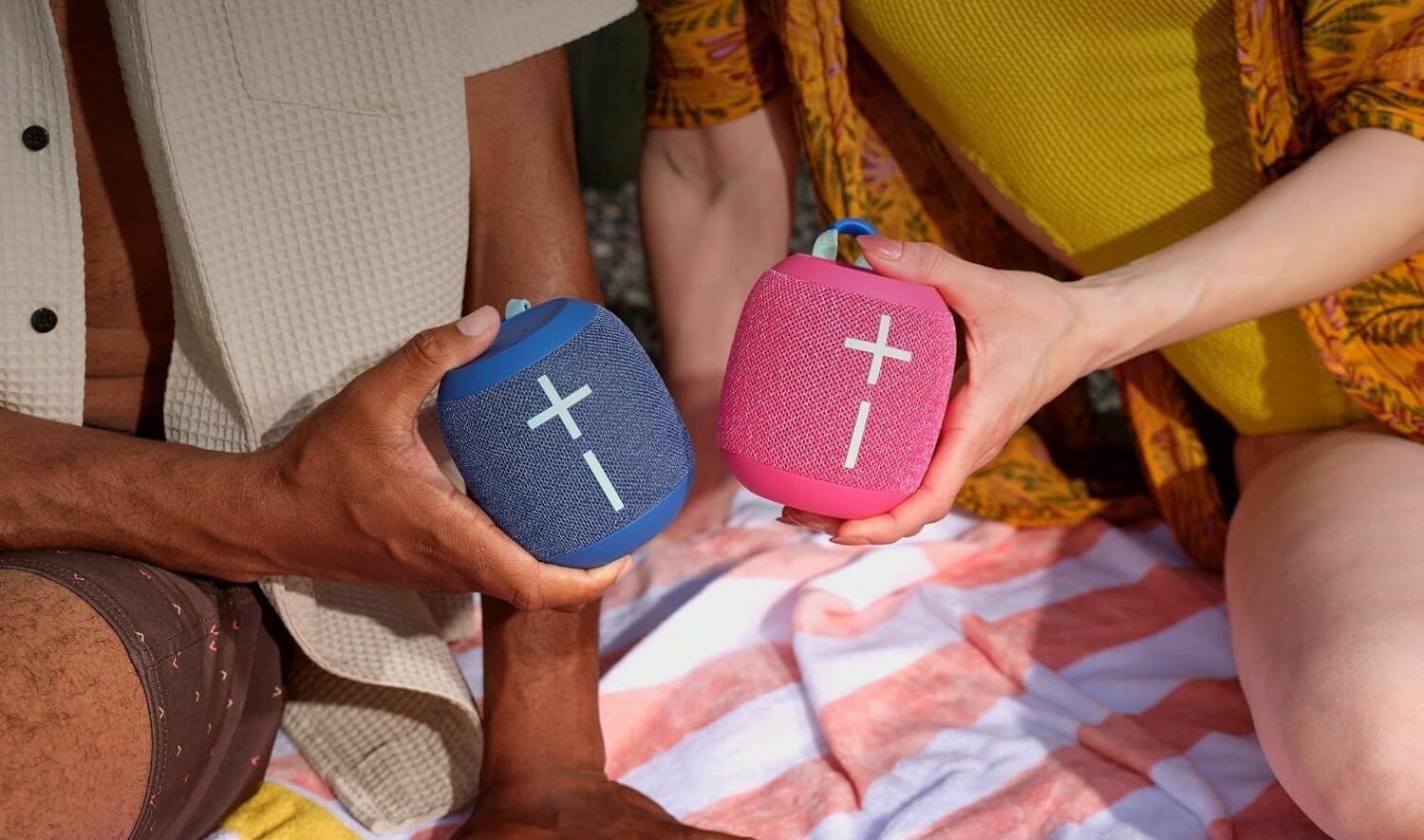 two people each hold an ultimate ears wonderboom 4 speaker while sitting on a picnic blanket