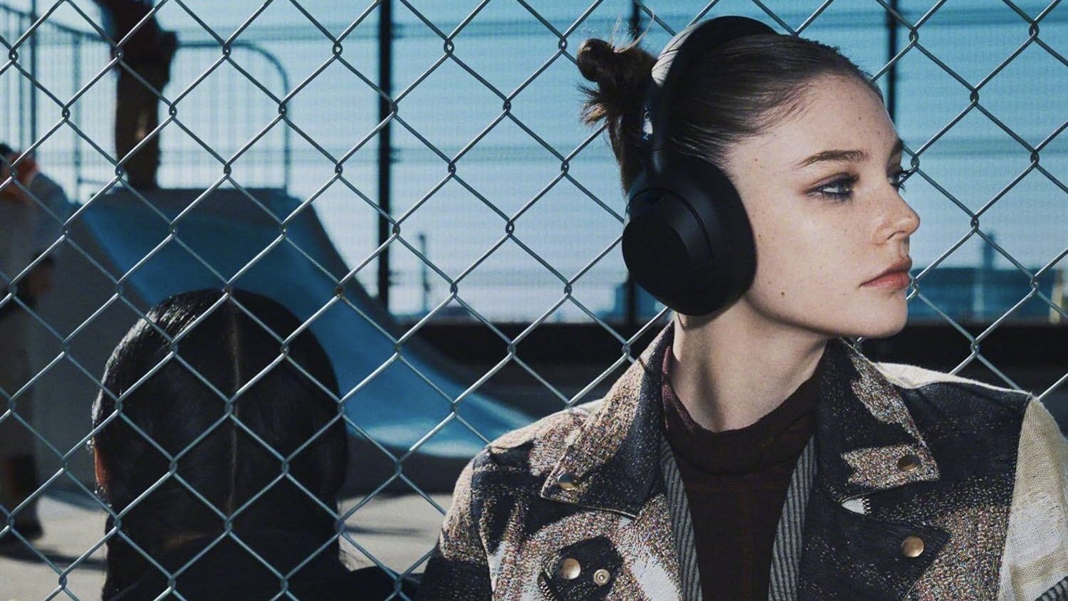 girl sitting in front of fence wearing black sony ult wear headphones