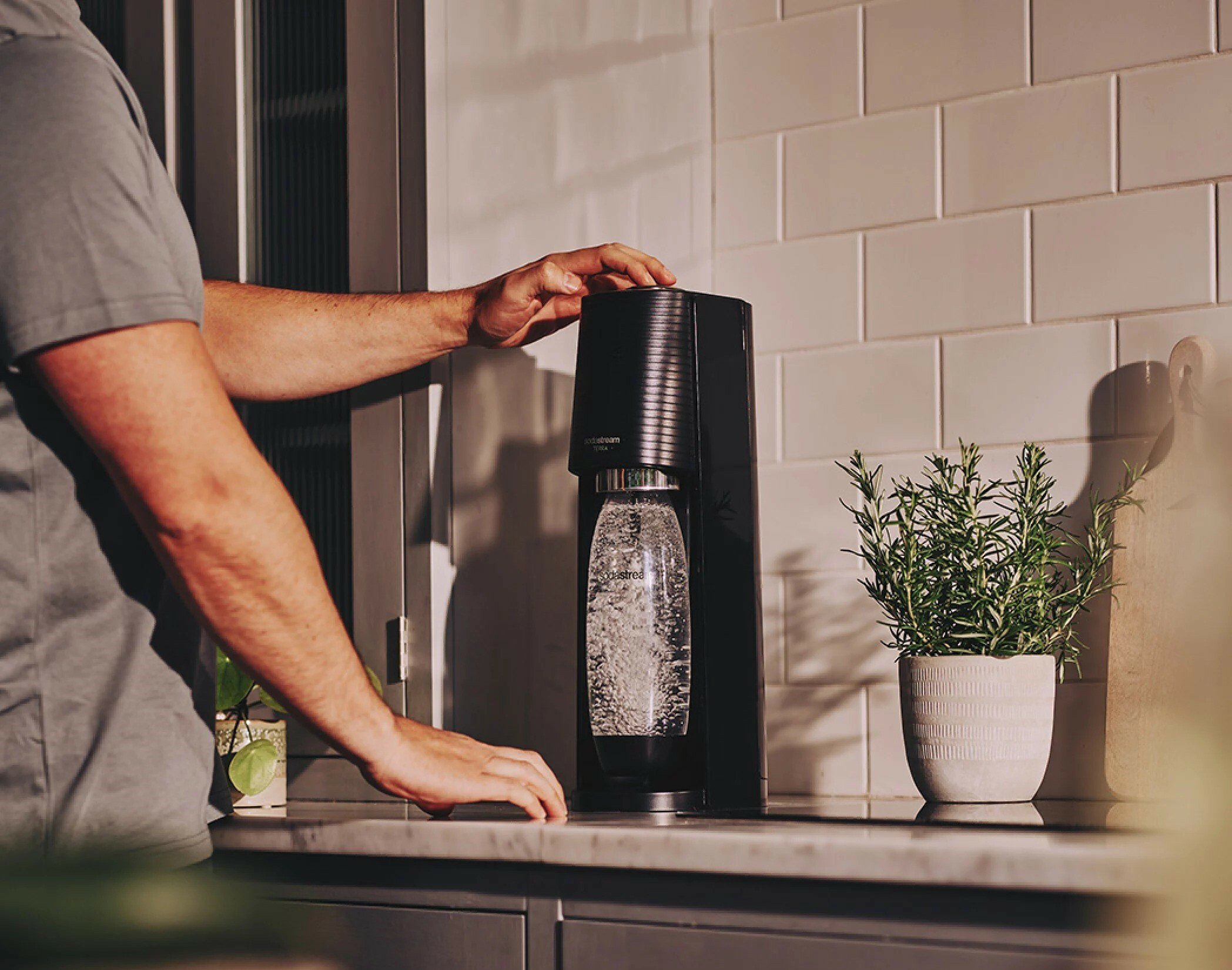 a person presses a button on the sodastream machine that sits on a counter