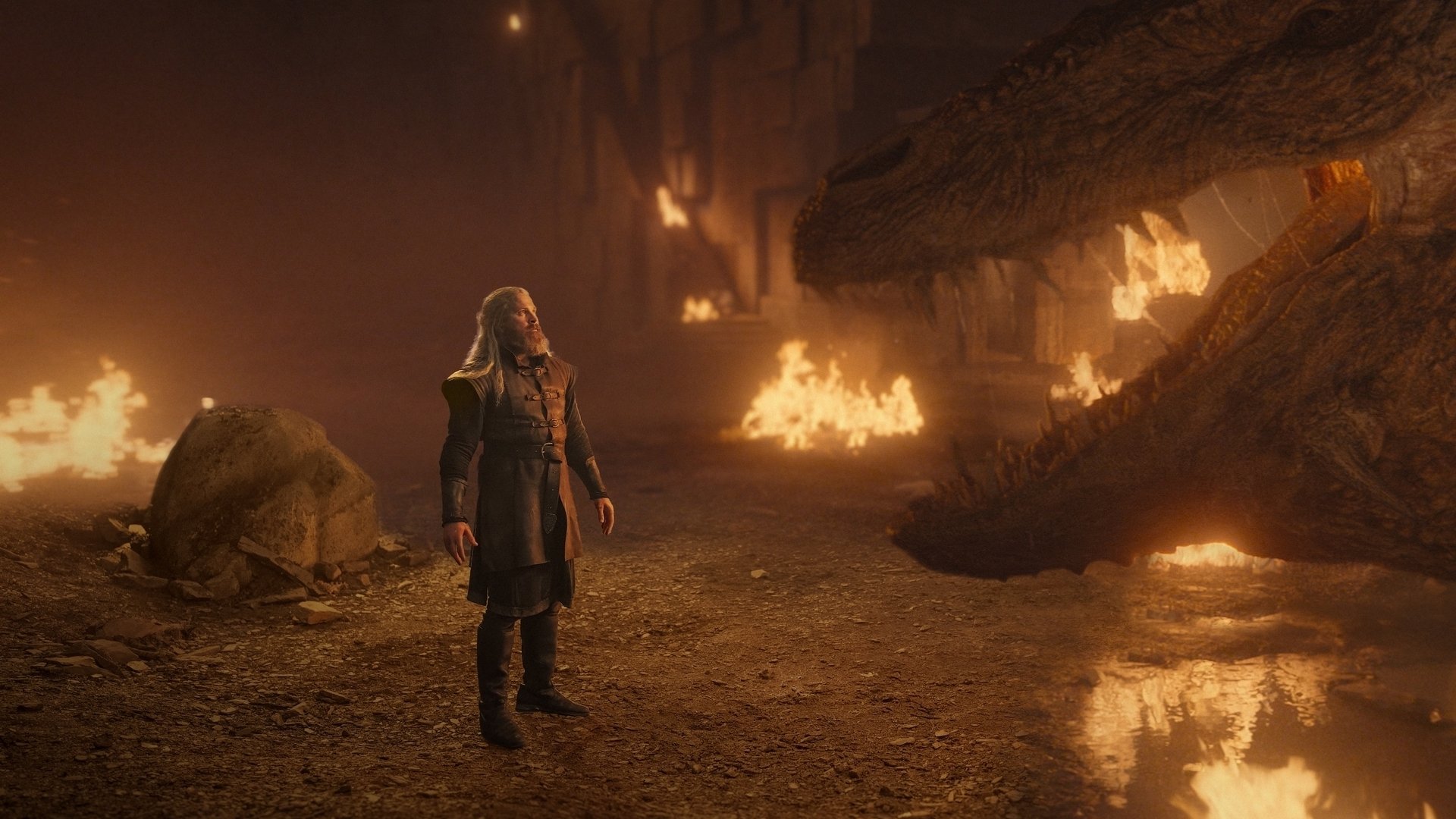 A man stands before a dragon in a fiery cavern.