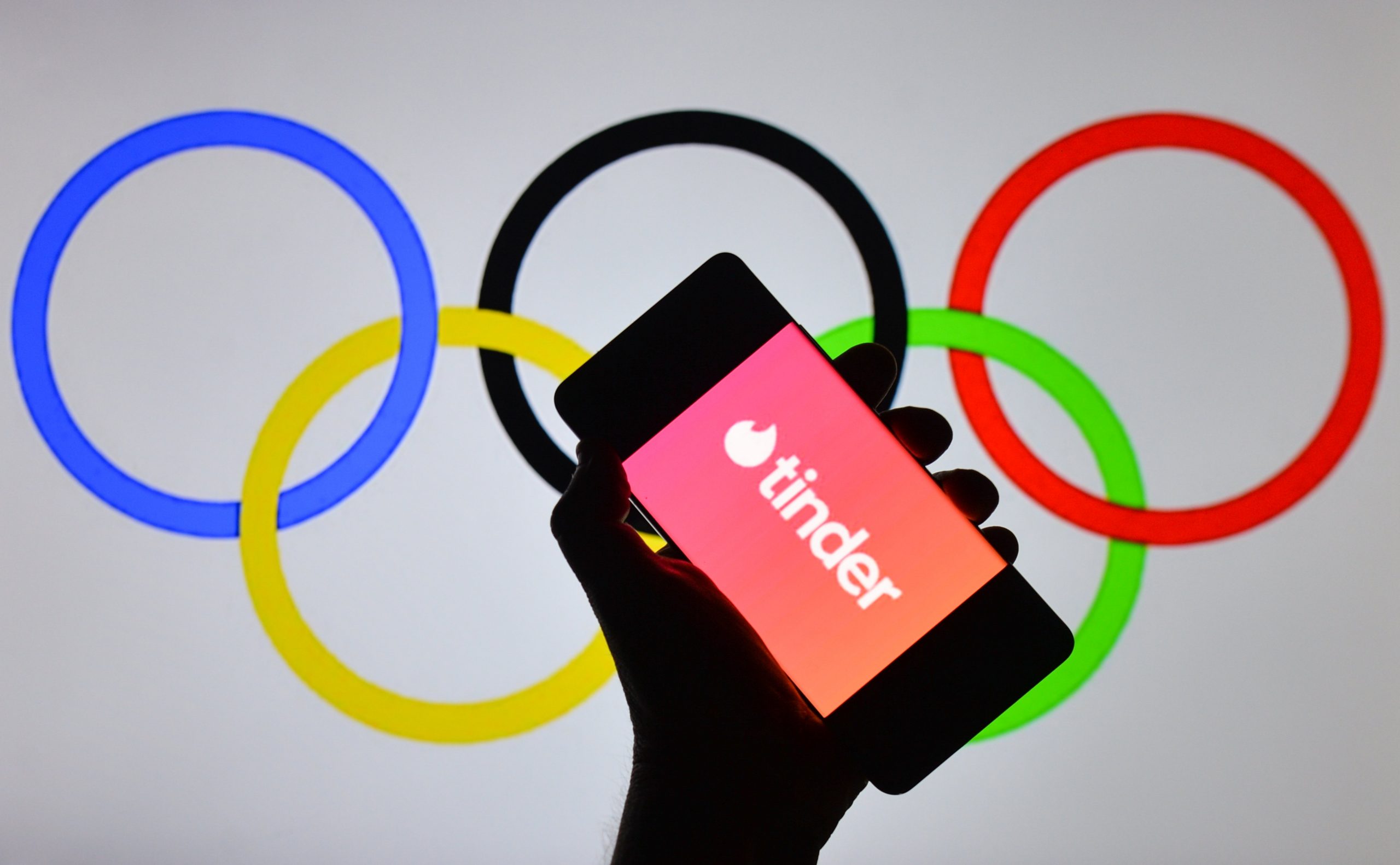 Tinder logo displayed on a mobile phone in front of Olympic Rings