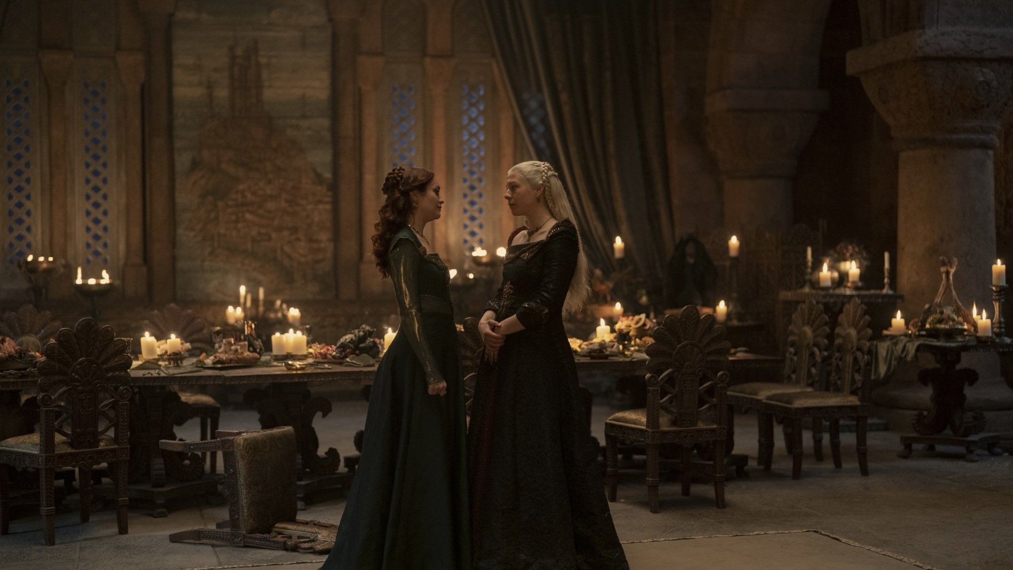 Alicent Hightower and Rhaenyra Targaryen have a discussion next to a banquet table in the Red Keep.