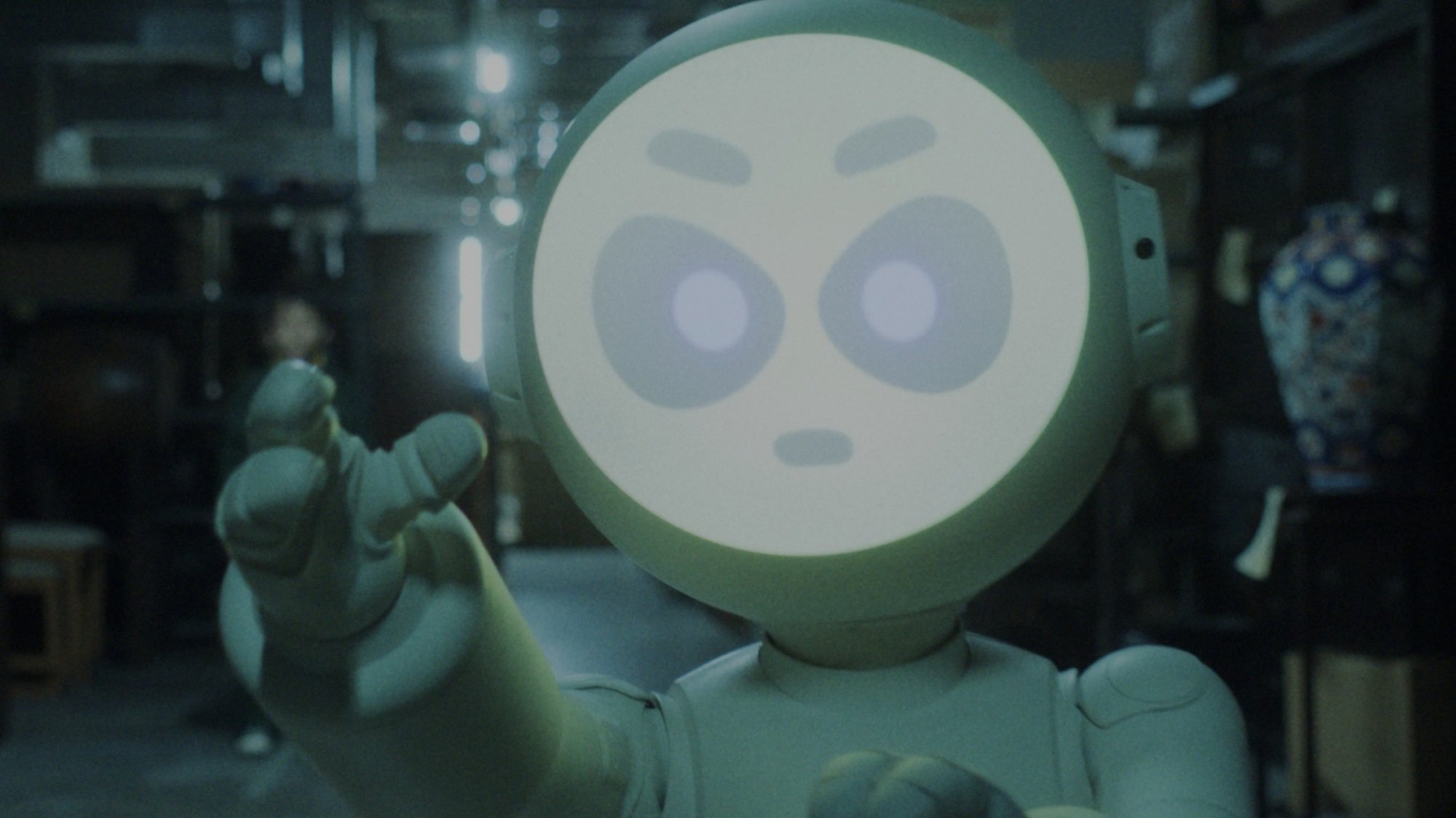 A white robot with a glowing, angry face holds out its hand in a threatening motion.